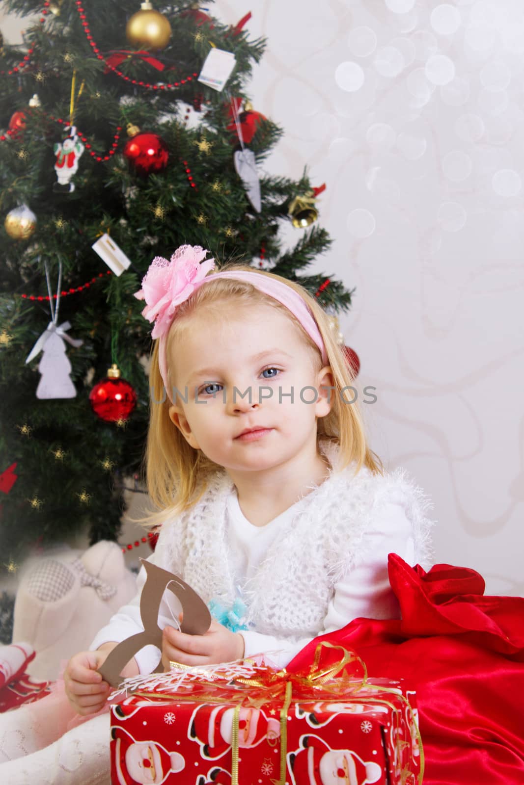 Adorable girl in pink under Christmas tree with gifts