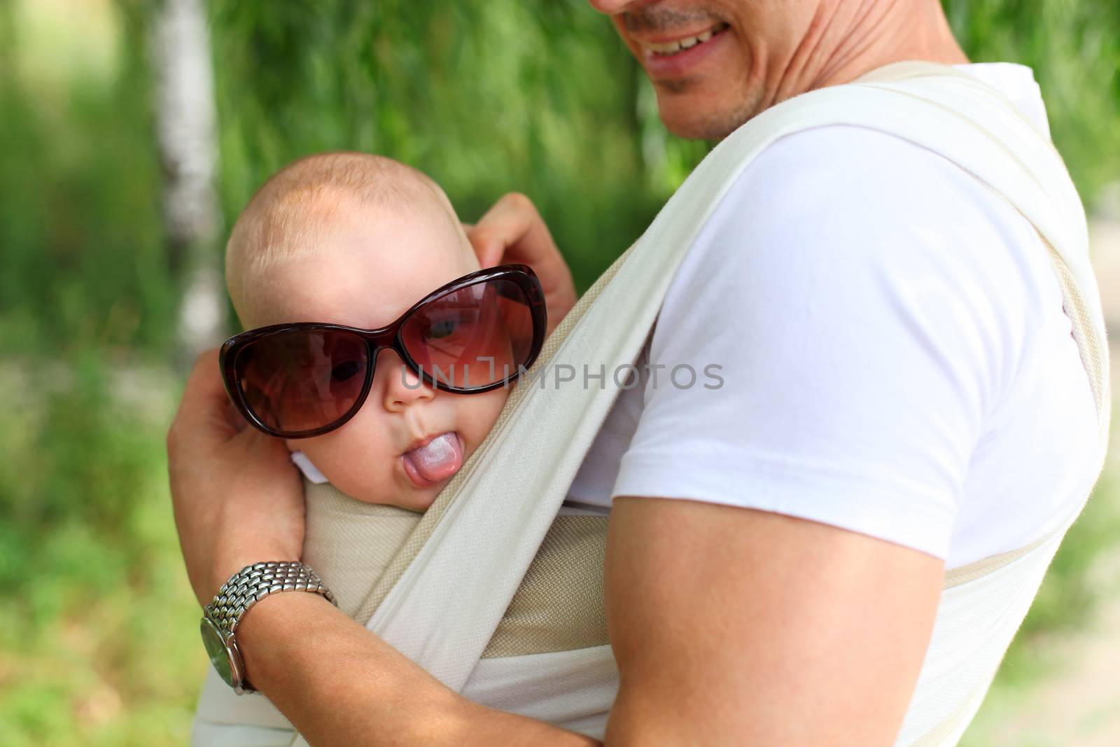 Closeup of baby boy in sling while his father is trying sunglasses on him, humorous aspect