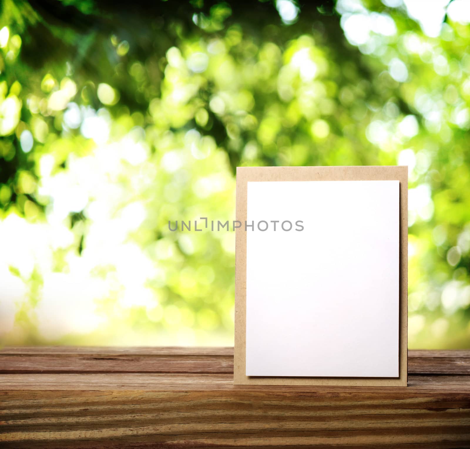 Greeting card on the wooden table over green tree leaves