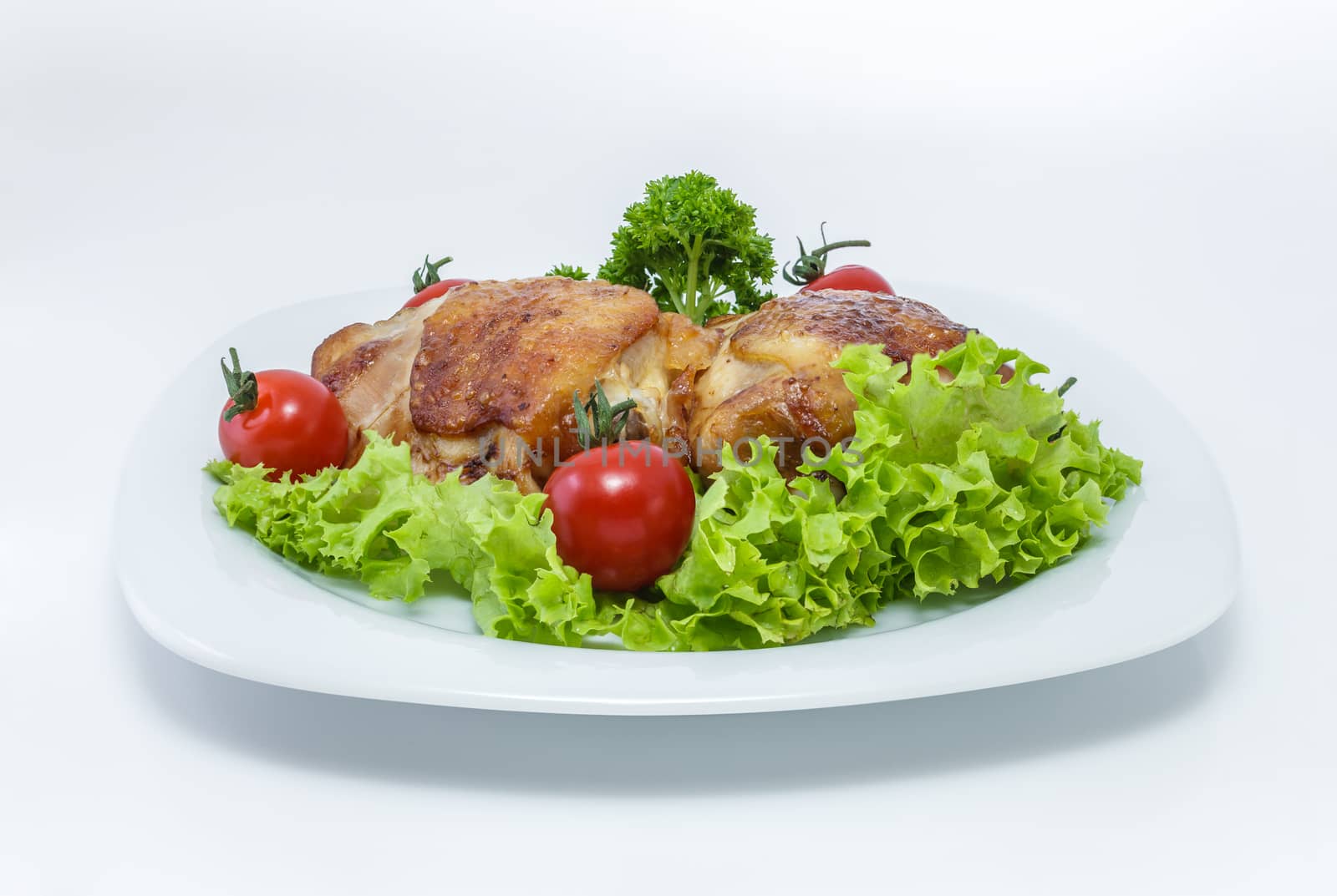 Fried chicken pieces on a plate with tomatoes, lettuce and parsley. Taken on a sheet of white plastic. Is not an isolate.