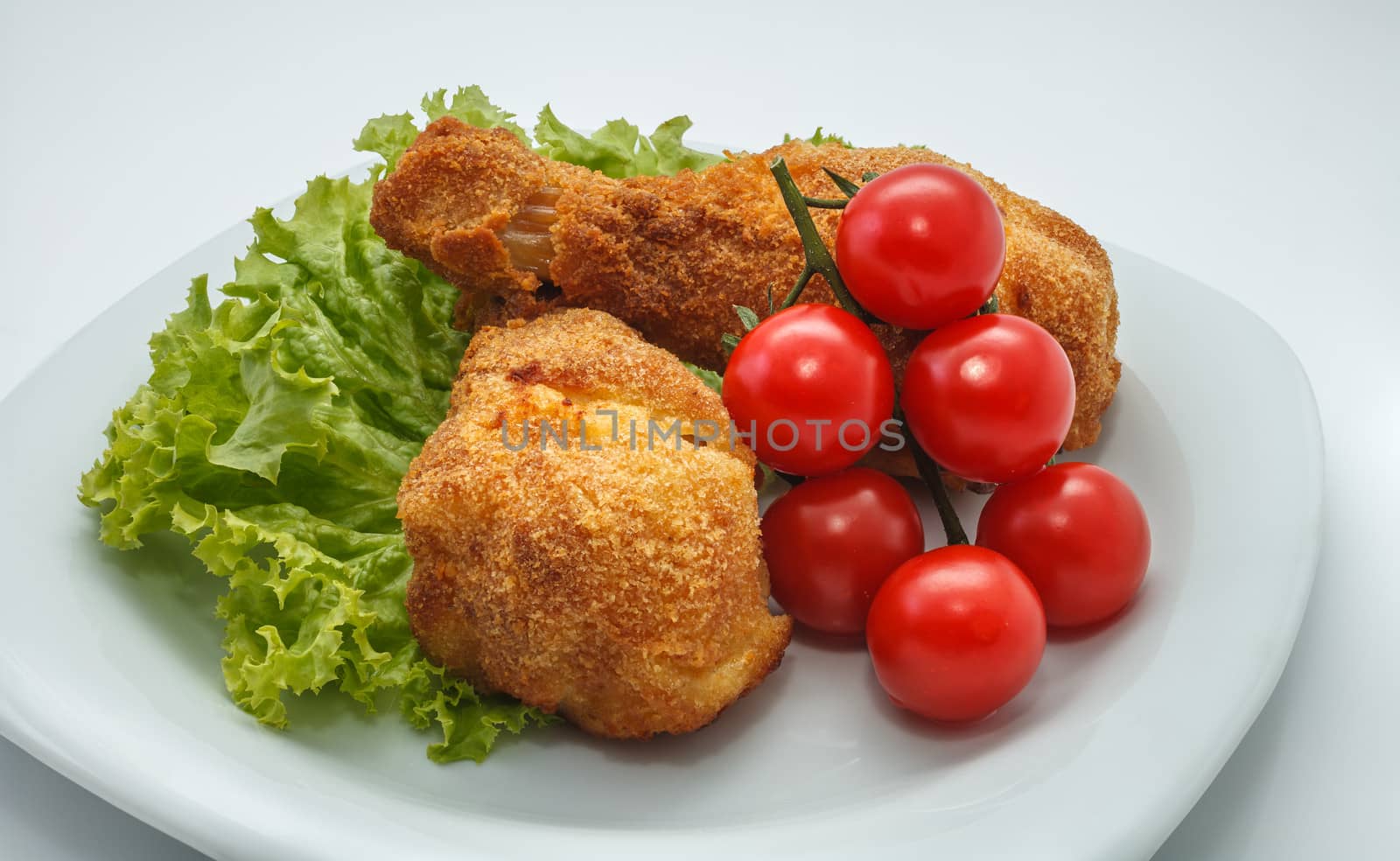 Fried chicken pieces on a plate with lettuce and tomatoes. Taken on a sheet of white plastic. Is not an isolate.