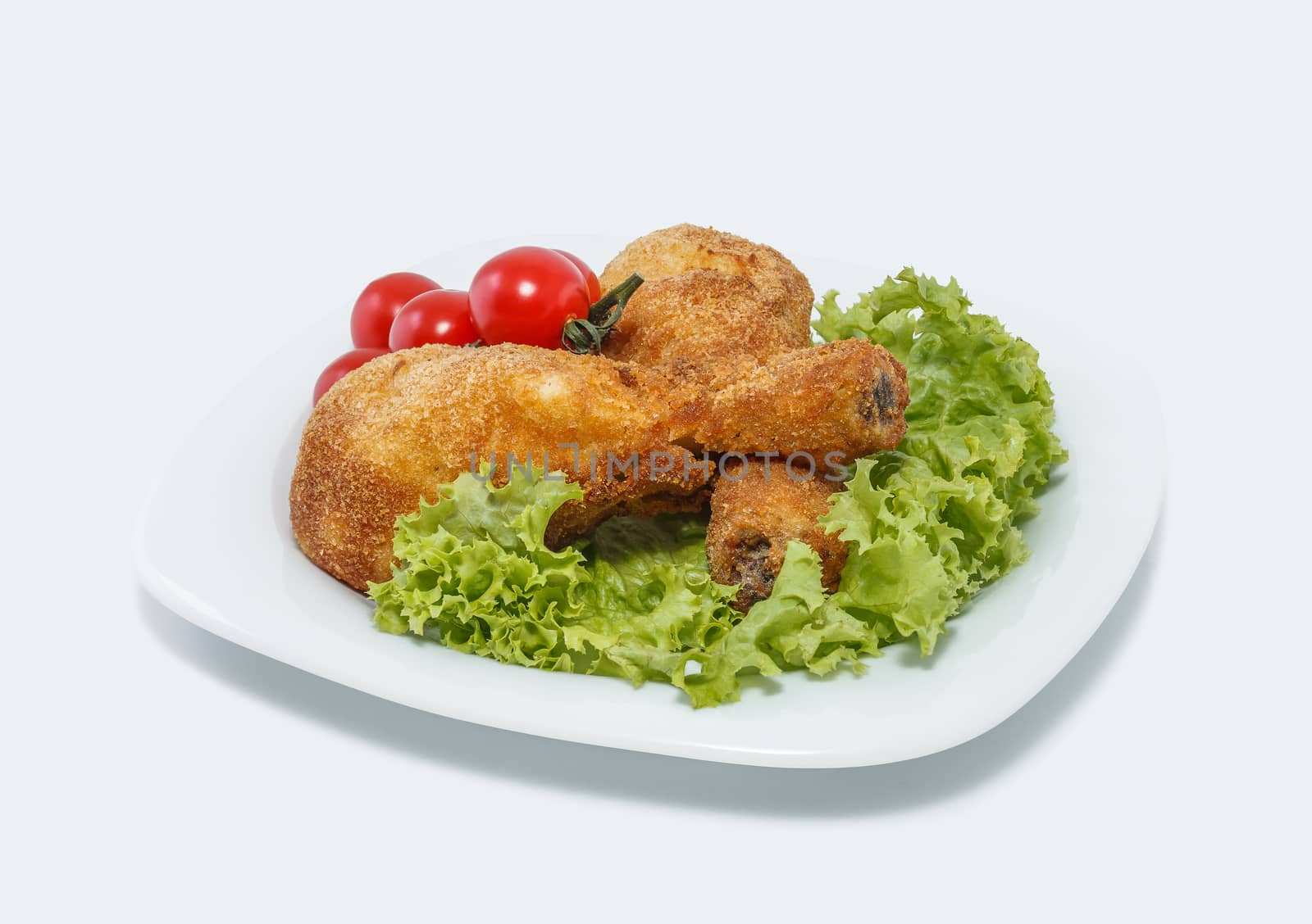 Fried chicken pieces on a plate with lettuce and tomatoes. Taken on a sheet of white plastic. Is not an isolate.