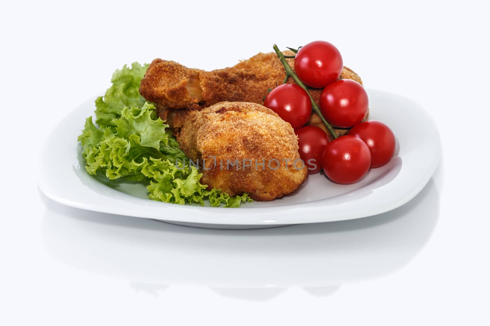 Fried chicken pieces on a plate with lettuce and tomatoes. Taken on a sheet of white plastic. Is not an isolate.