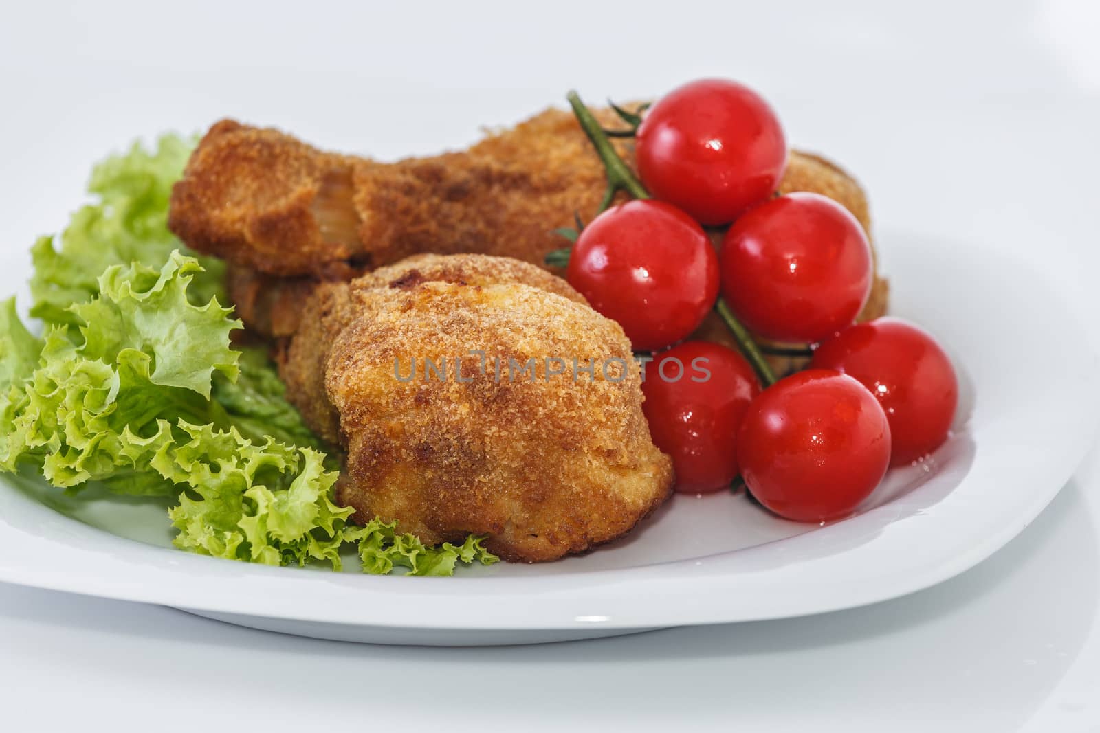 Fried chicken pieces on a plate with lettuce and tomatoes. Taken on a sheet of white plastic. Is not an isolate.