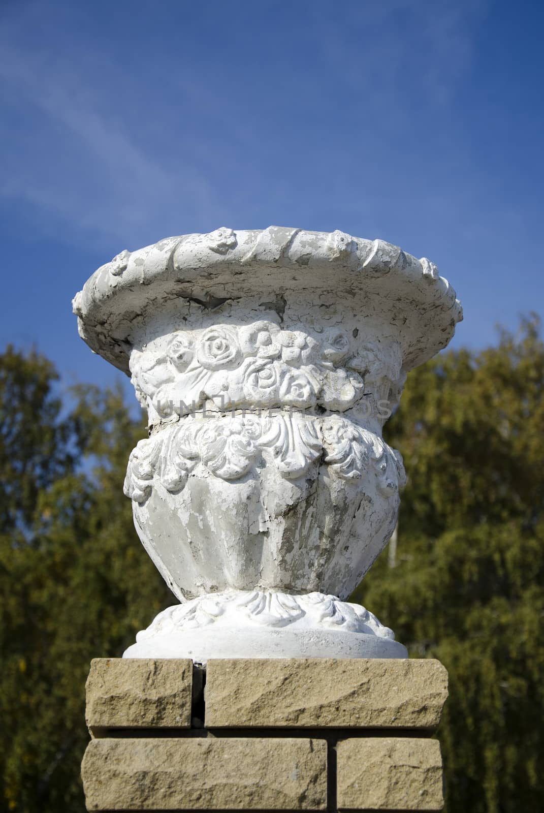 The Old plaster garden vase on a modern brick pedestal on tree background