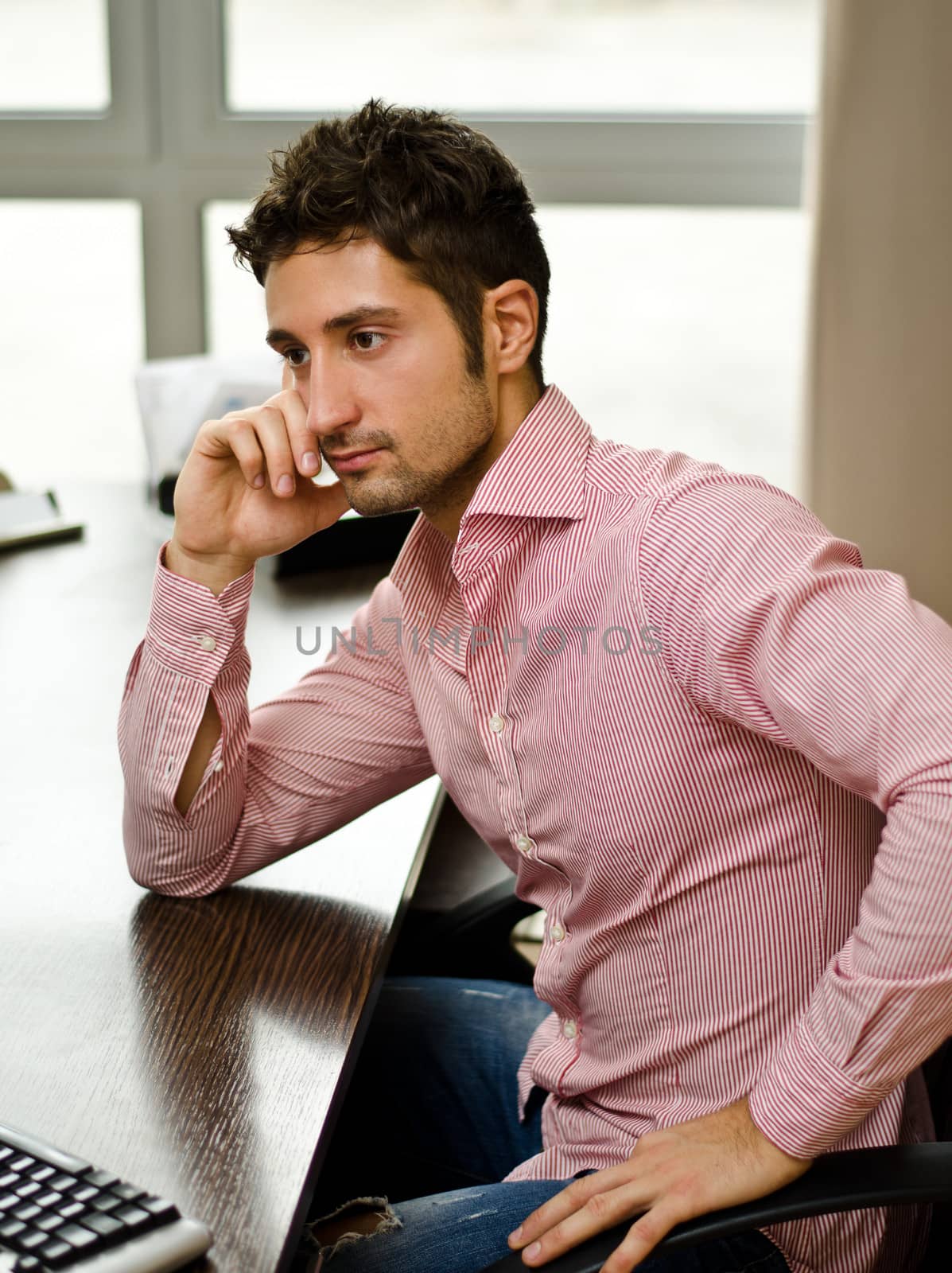 Attractive young businessman sitting at desk in his office in front of computer