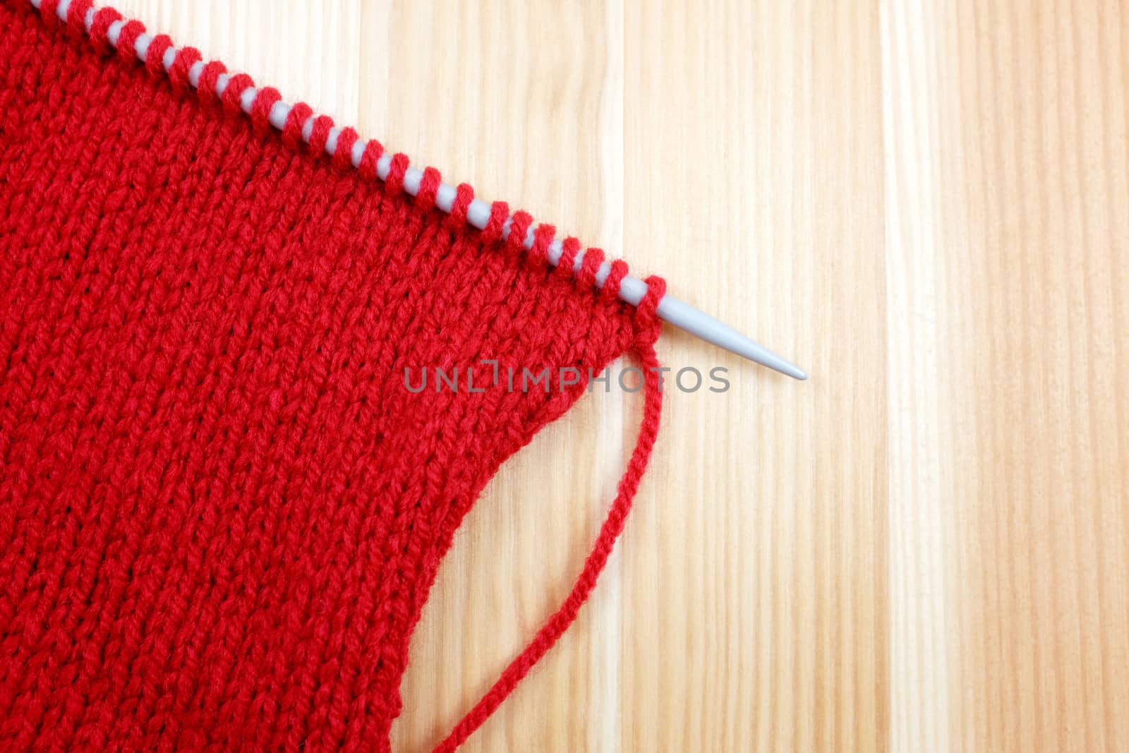 Stockinette stitch in red wool on a knitting needle, on wooden background