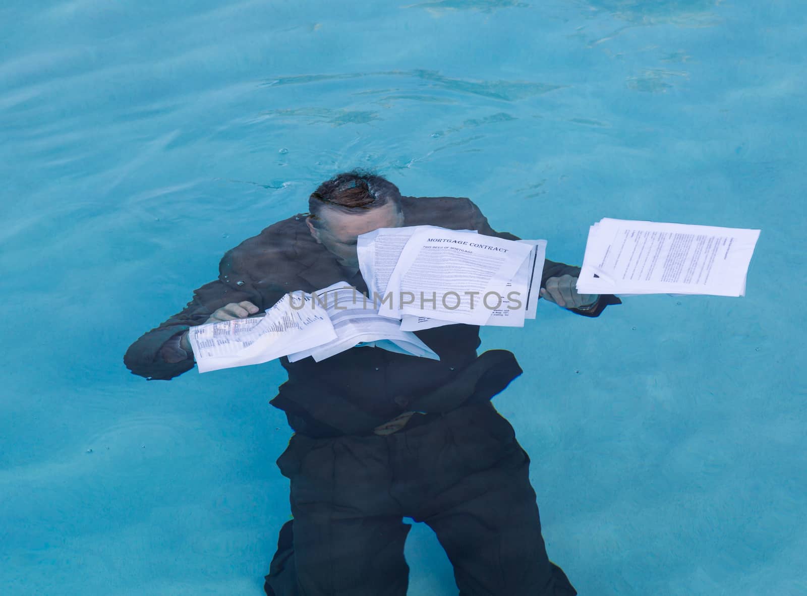 Senior caucasian businessman in suit sinking underwater in deep blue pool worried about being underwater with mortgage payments