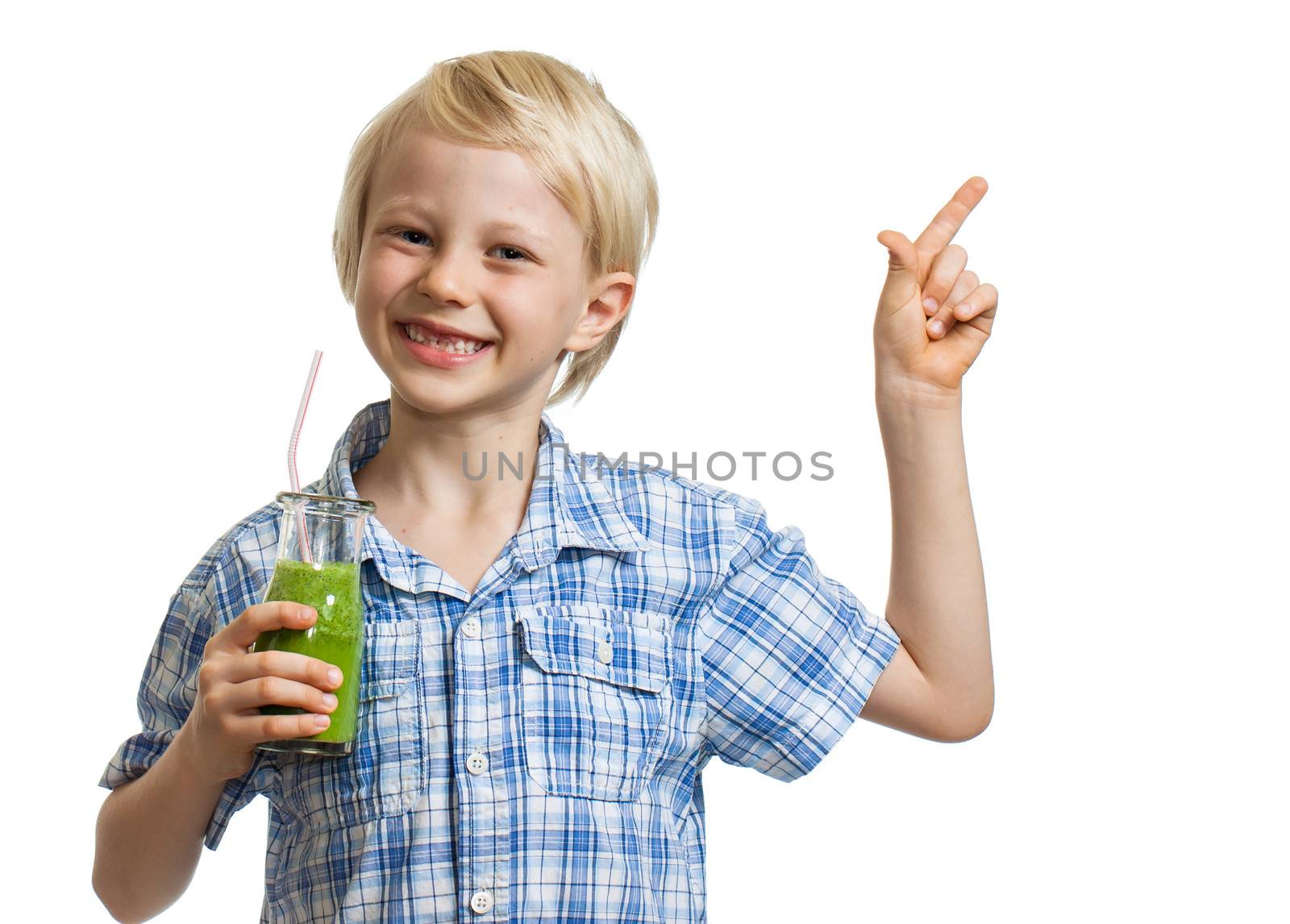 A cute young healthy boy holding green smoothie, smiling and pointing at copy-space. Isolated on white.