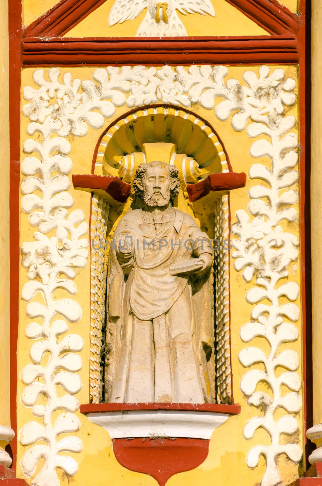 A small statue on the exterior of an old yellow church in souther Mexico