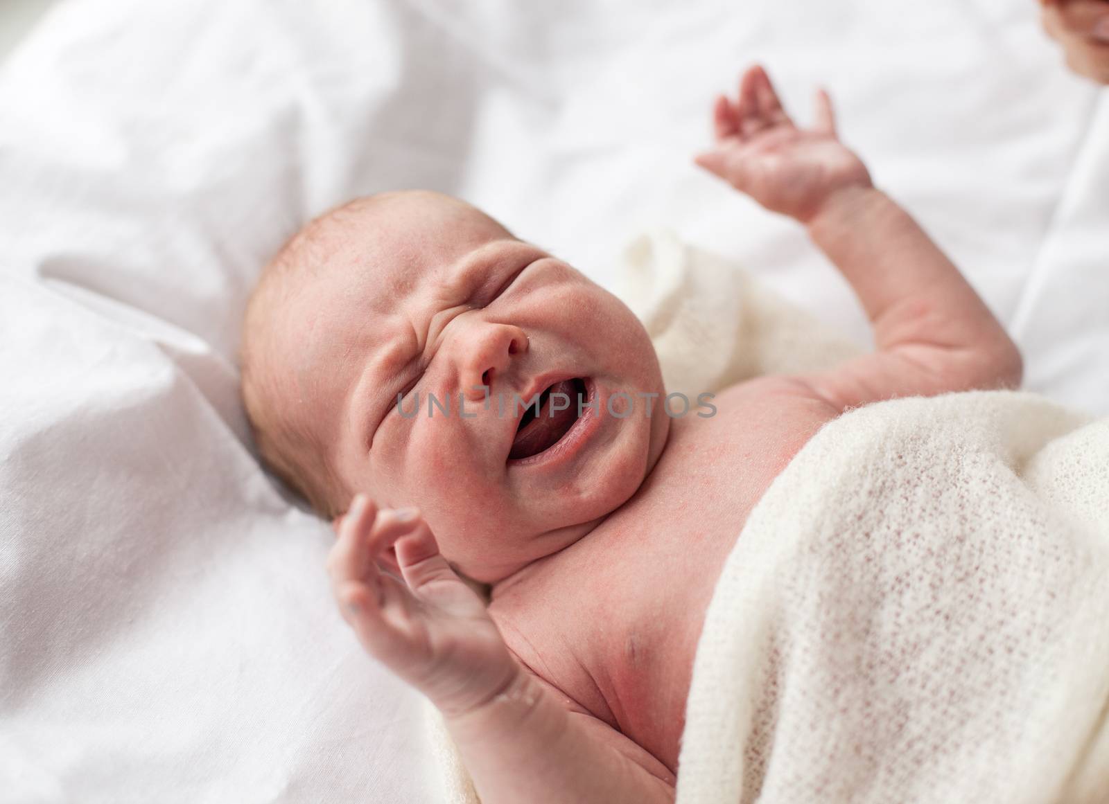 Closeup of newborn baby crying lying down on bed