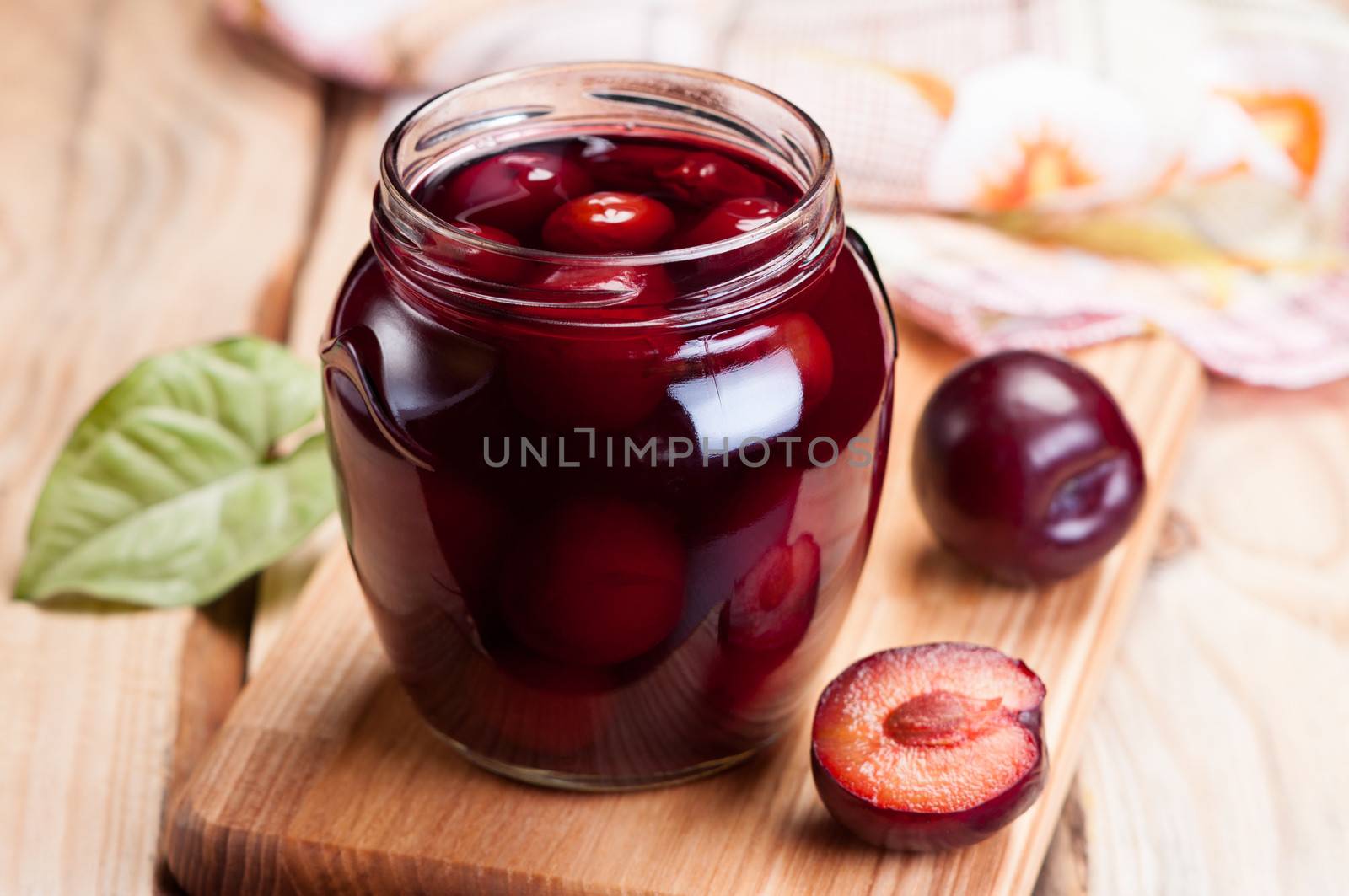 Homemade plum jam in glass jar on wooden table.