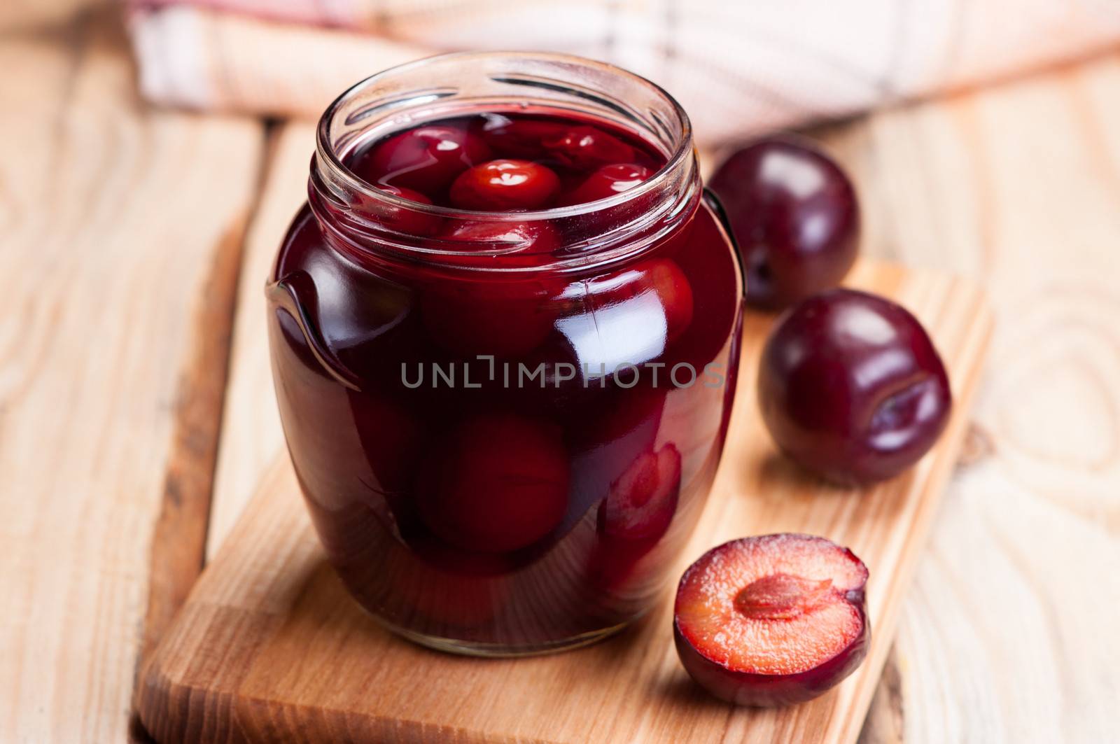Plum compote in glass jar on wooden table.