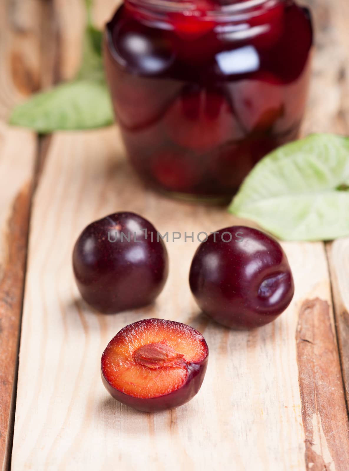 Plums on rough wooden table close-up. In background glass jar with jam.