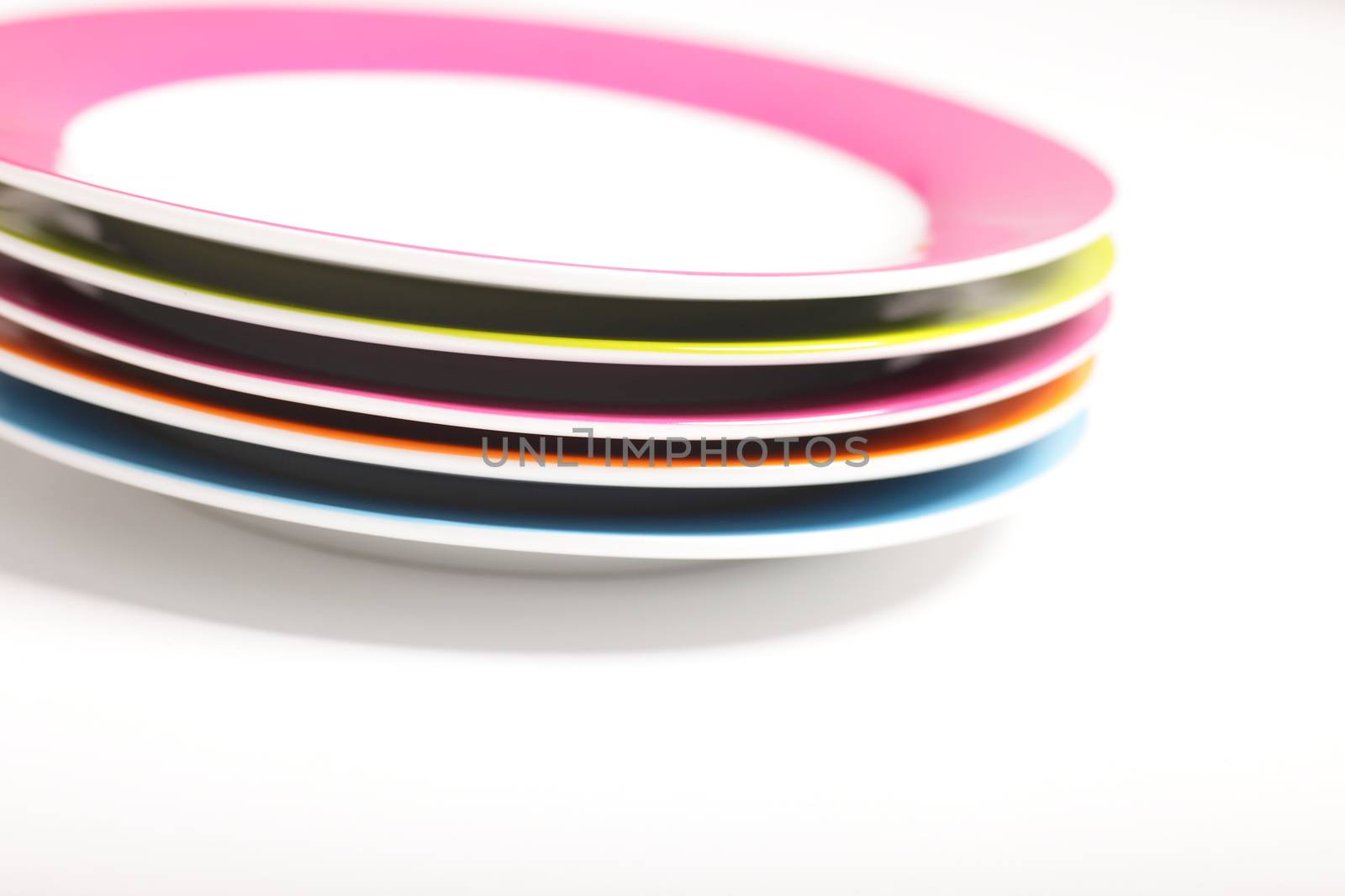 Stack of colourful empty plates with multicoloured borders for catering and serving food on a white background
