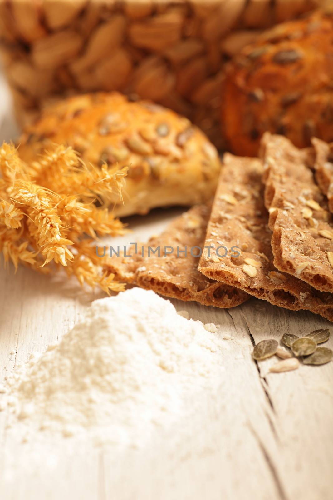 Still life display of wheat ingredients and products including ground flour, ears of ripe wheat, crispbread and delicious freshly baked golden rolls