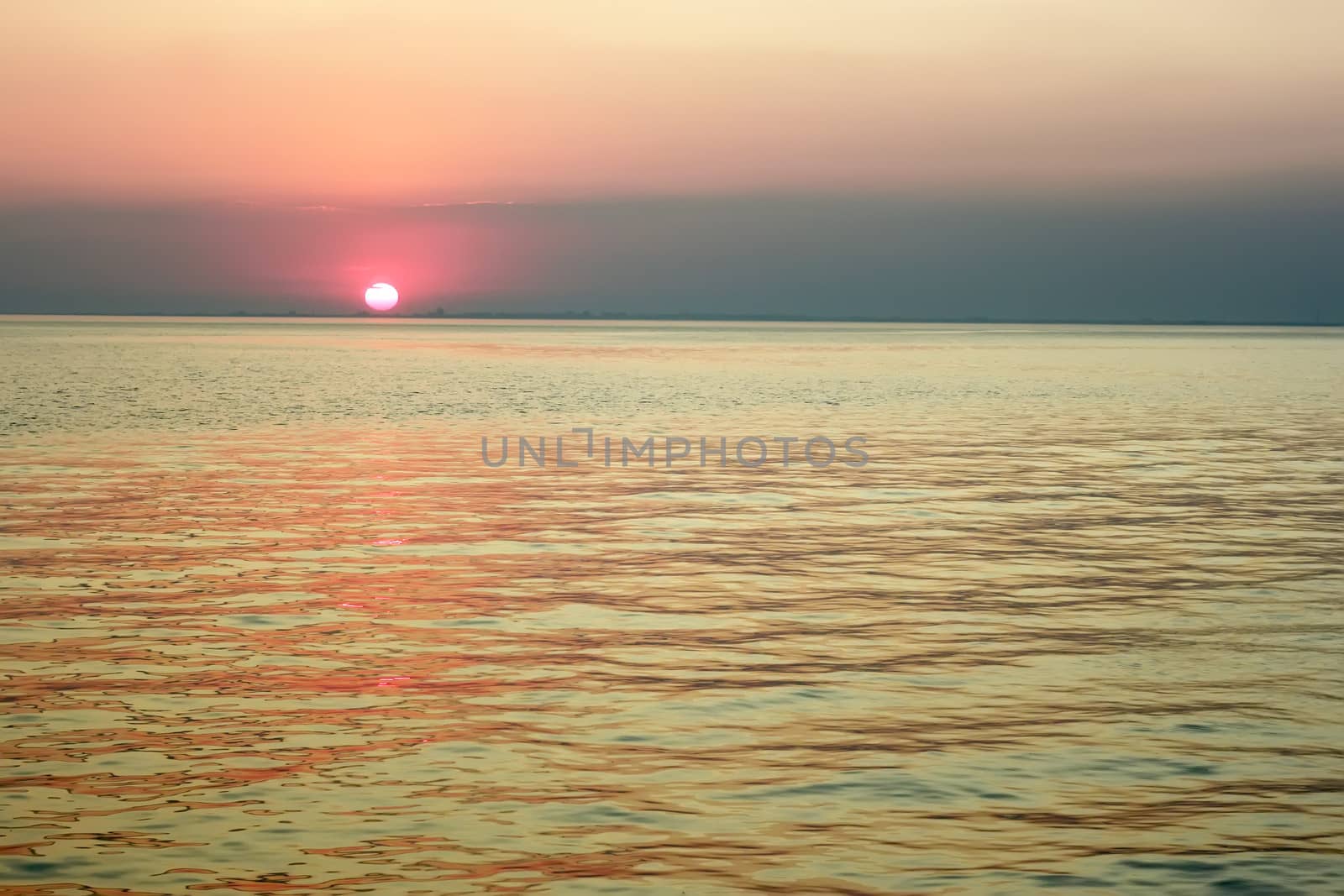 Red sun in the clouds near the horizon over the sea bay