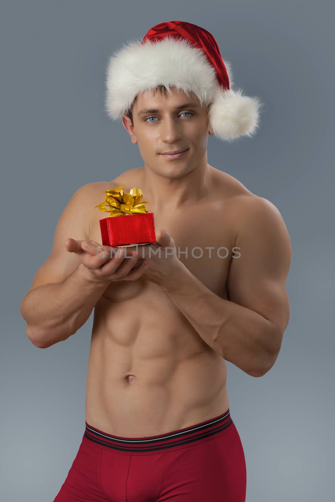 Sexy muscular man in santa cap holding smal gift