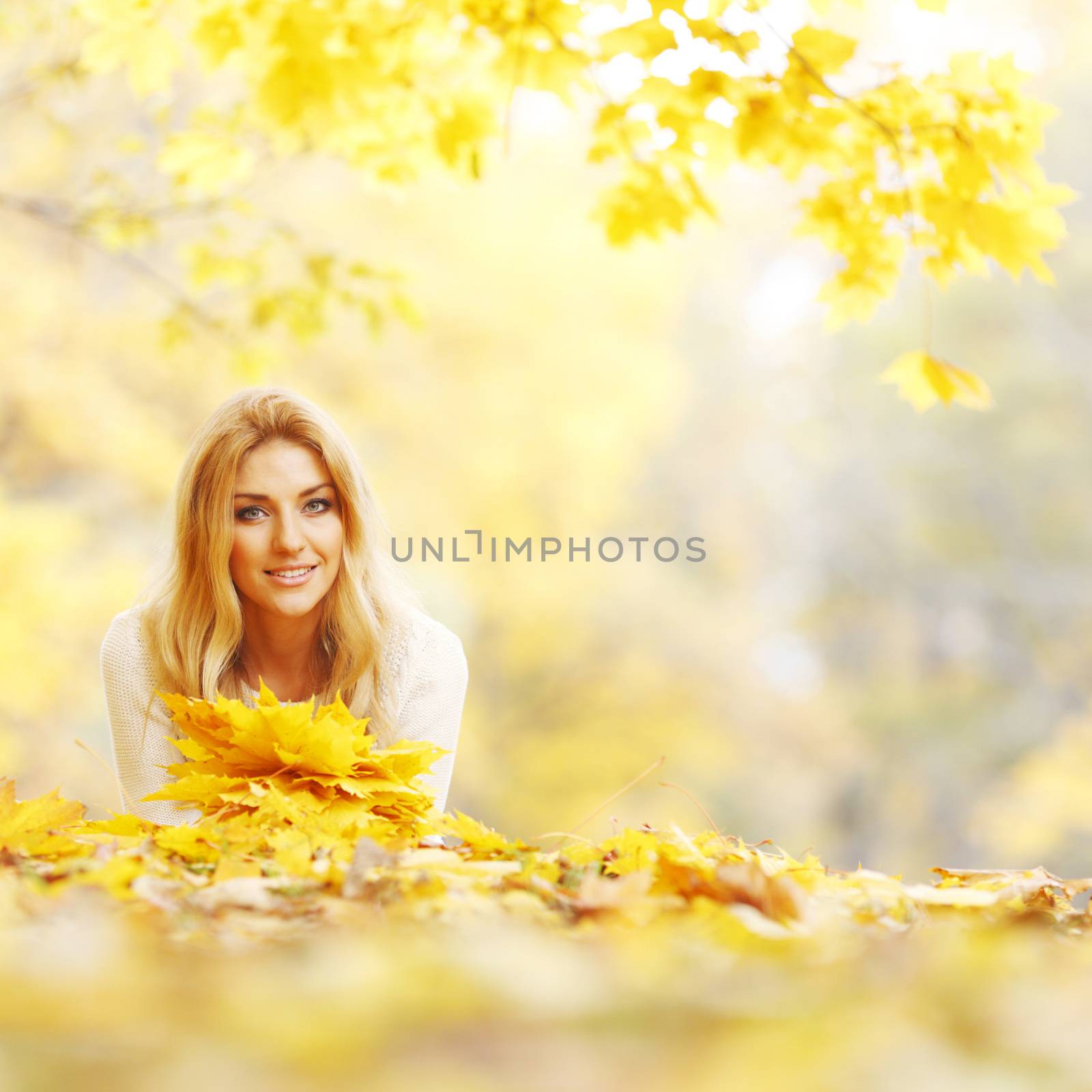 Young woman laying down on the ground covered dry autumnal foliage in beautiful park