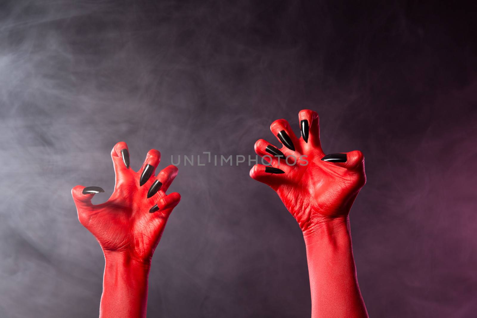 Spooky red devil hands with black glossy nails, Halloween theme, studio shot over smoky background 