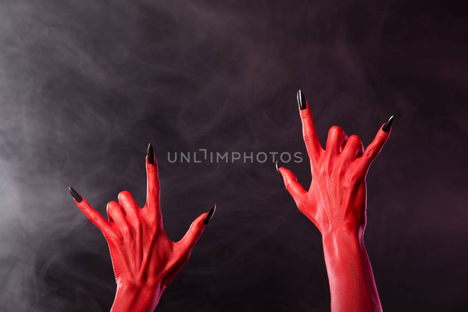 Red devil hands showing heavy metal gesture, studio shot on smoky background 