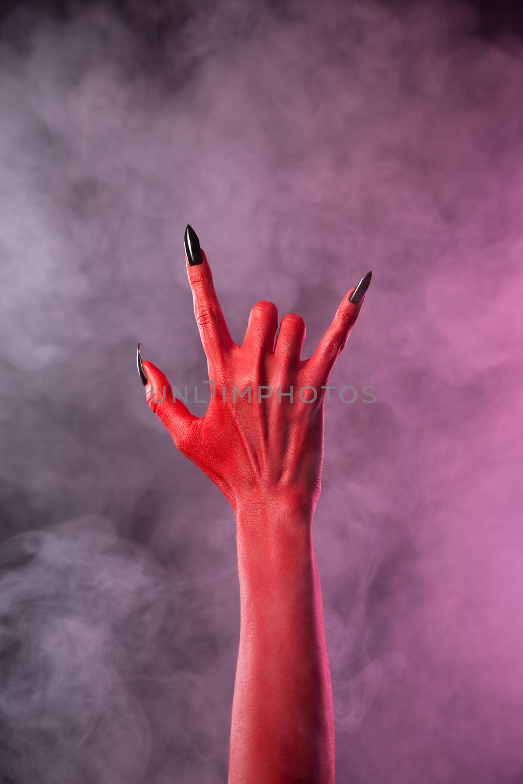 Spooky devil hand showing heavy metal gesture, studio shot on smoky background 