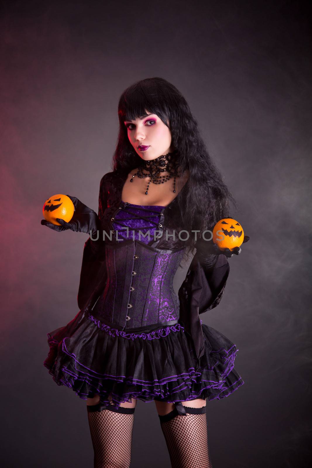 Pretty witch in purple Halloween costume holding Jack-o-lantern style oranges 