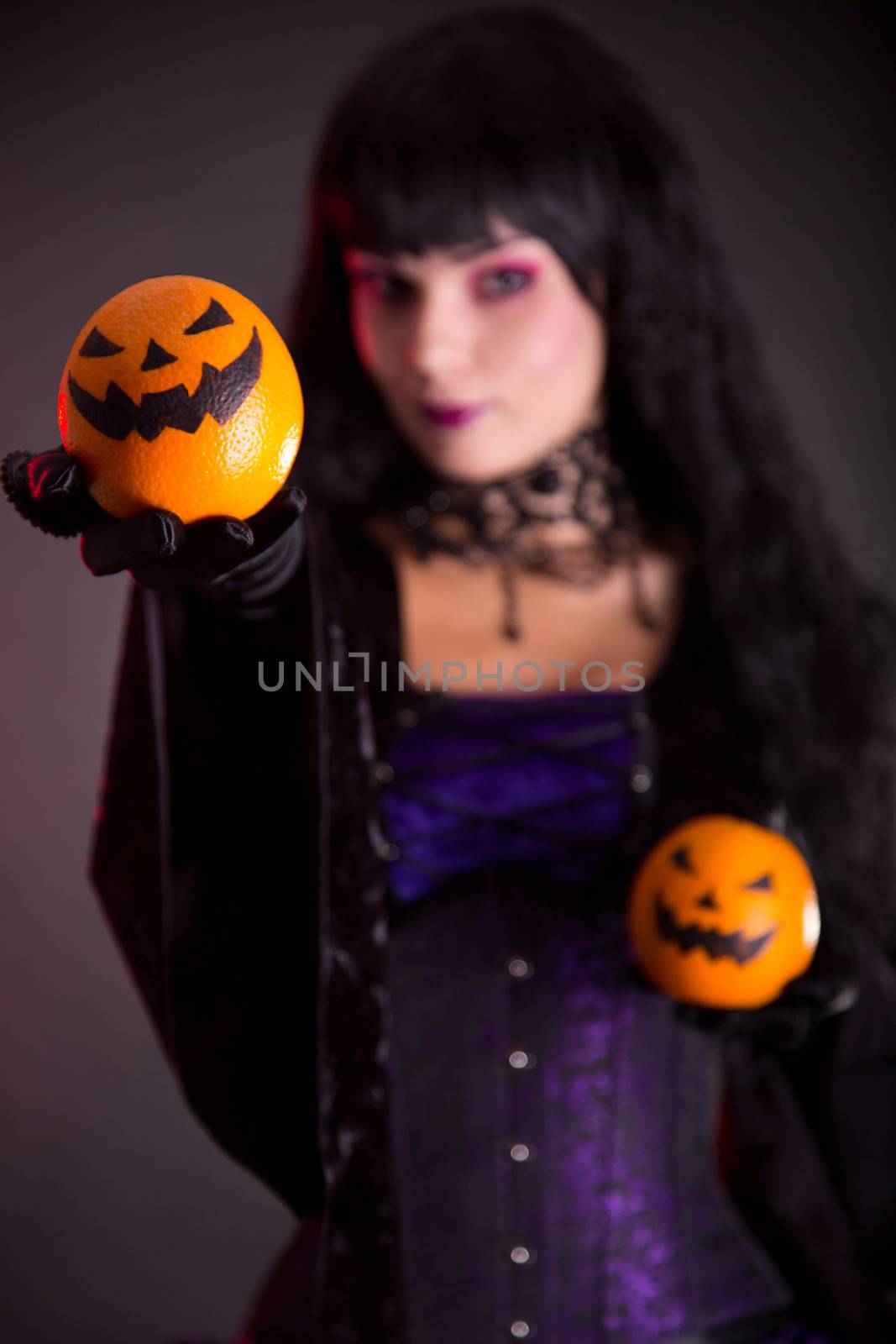 Pretty witch holding Jack o lantern oranges, selective focus on fruits 