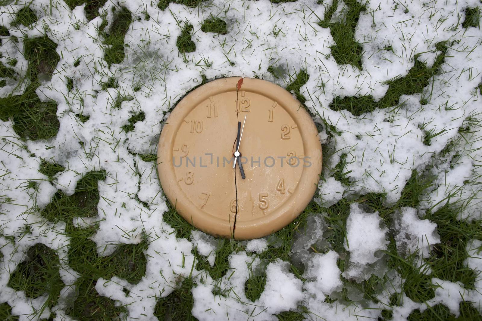 a broken clock face in the snow covered grass as if frozen in time and time has stopped