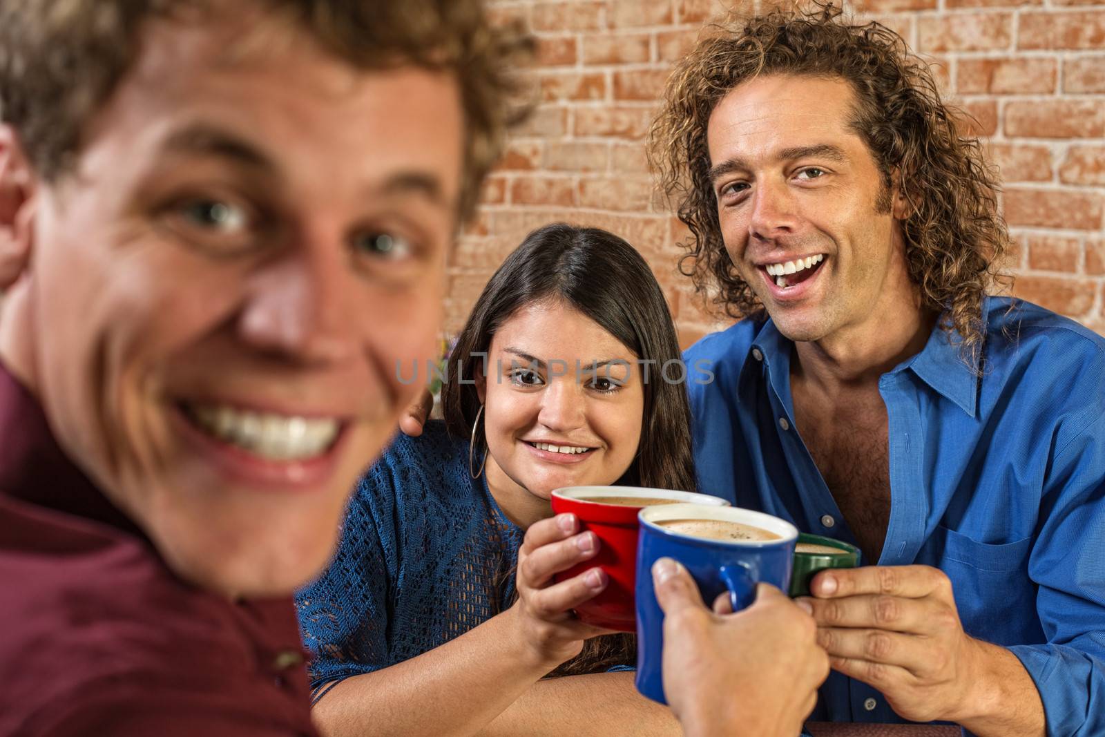 Excited friends toasting with coffee mugs in cafe