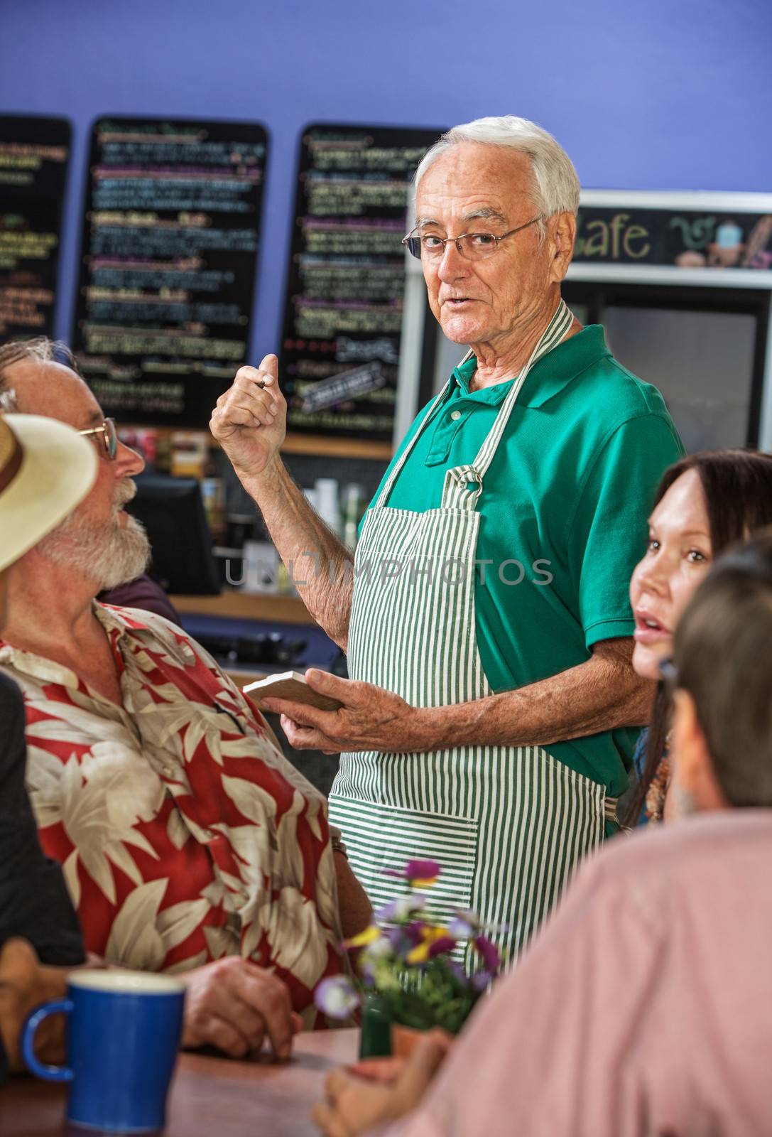 Cafe barista pointing to menu with group of customers
