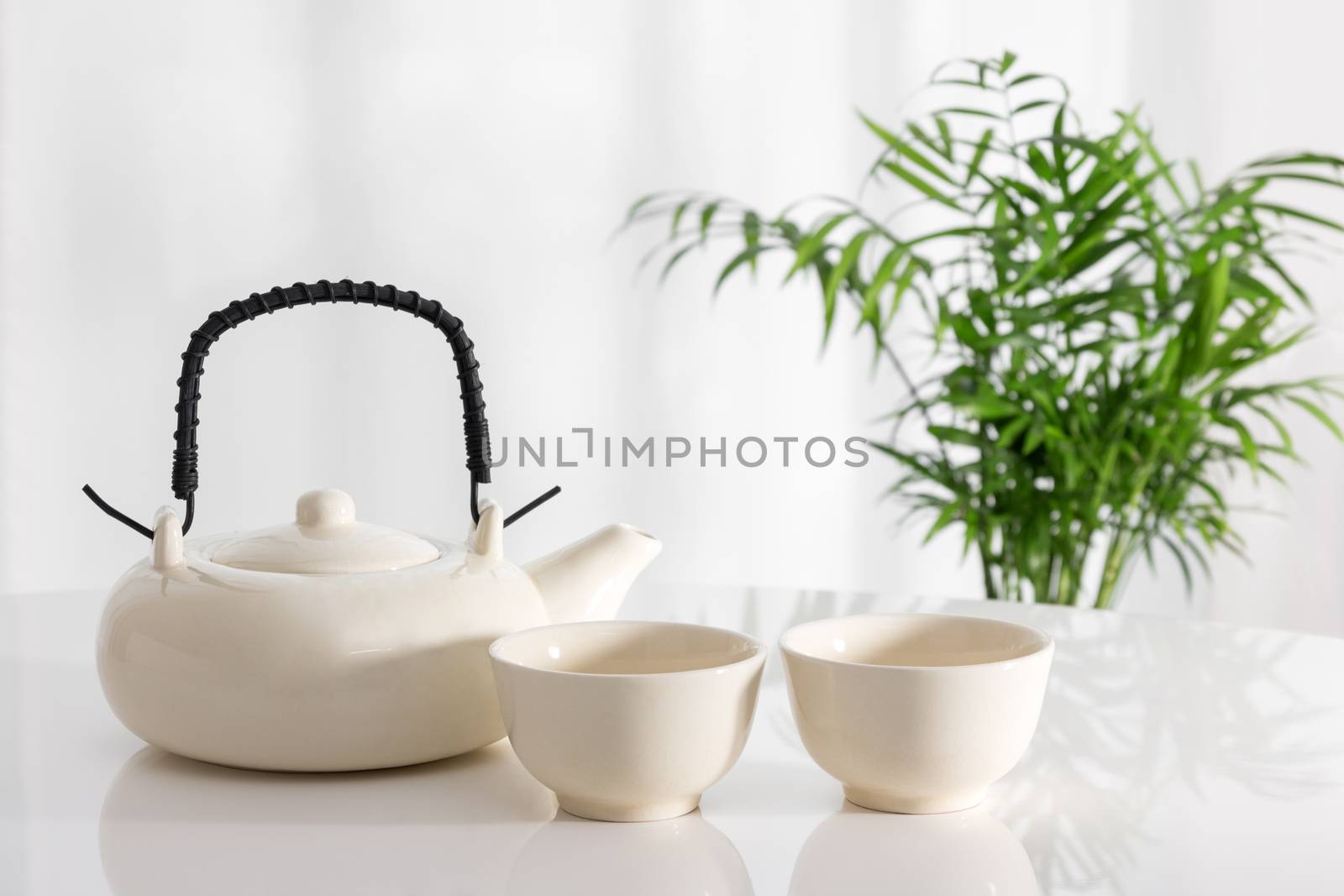 White ceramic teapot and cups on the table, with green plant in the background.