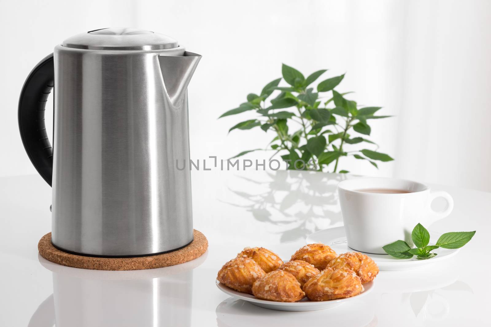 Teatime. Electric kettle, teacup and cookies on a table.