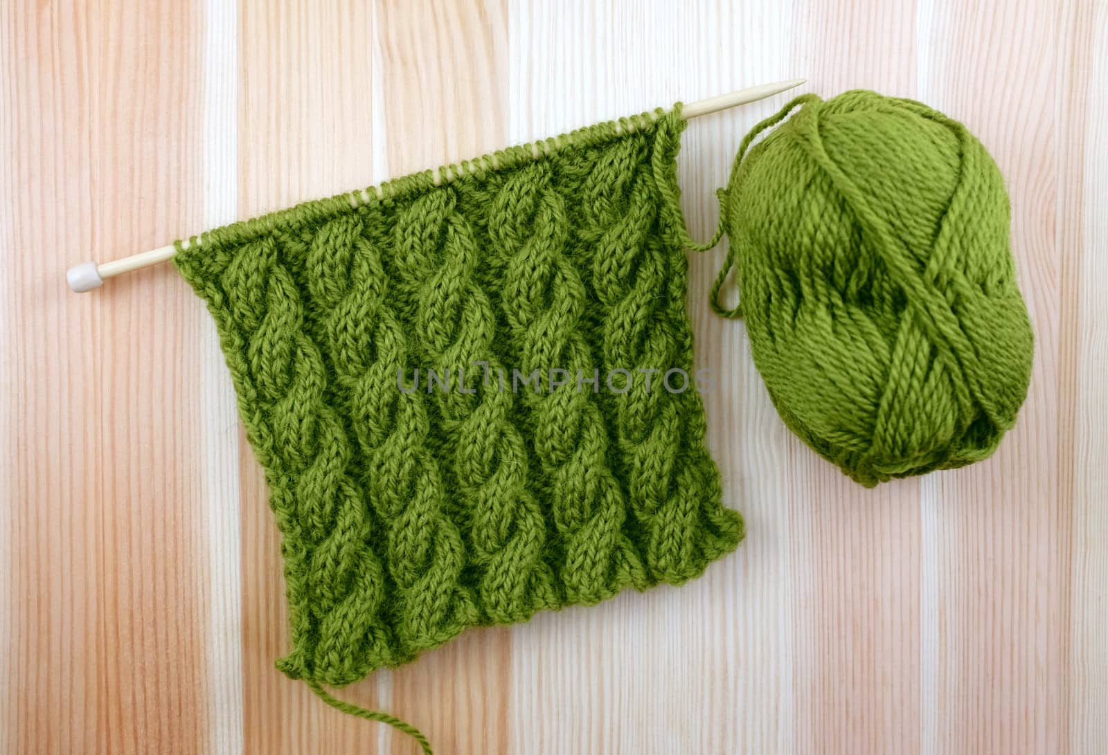 Rich green coiled rope cable stitch knitting with a ball of wool on woodgrain