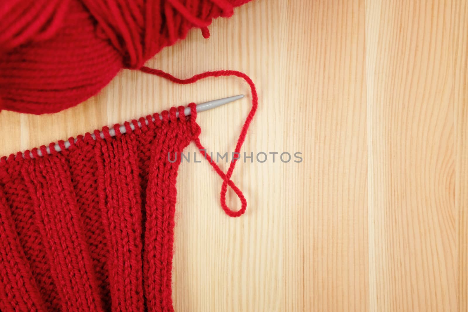 Red rib stitch on the knitting needle with a ball of wool, on wood