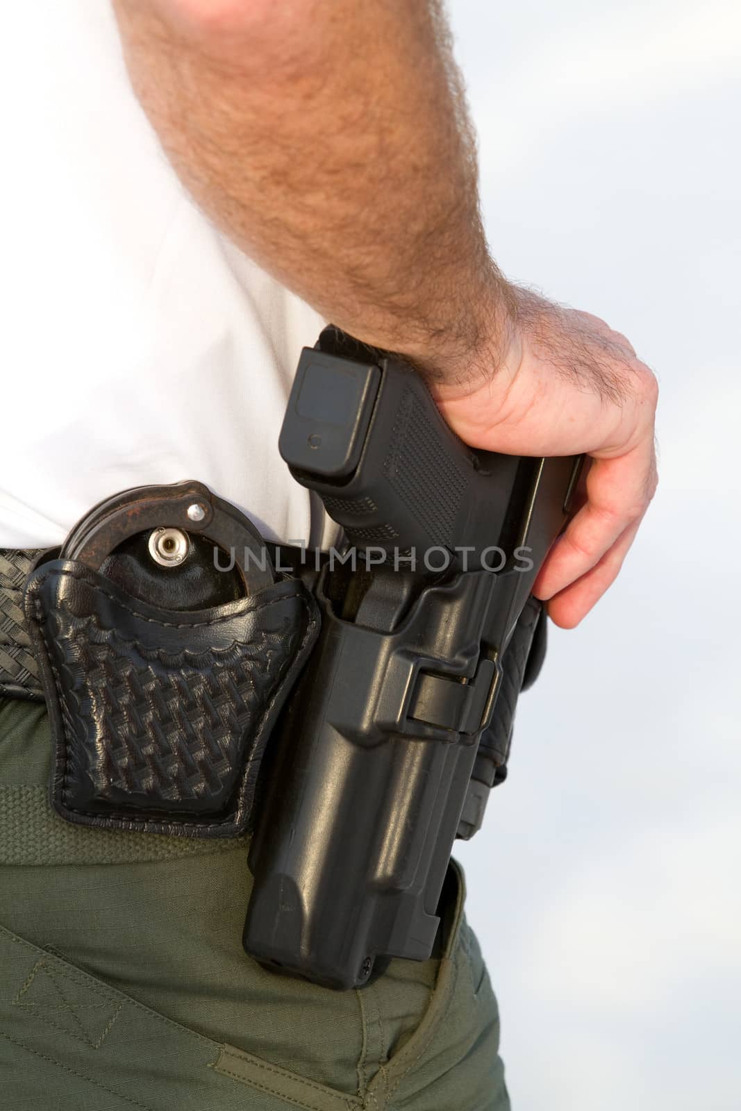 Police officer rests his hand on his weapon belt which also holds his handcuffs.