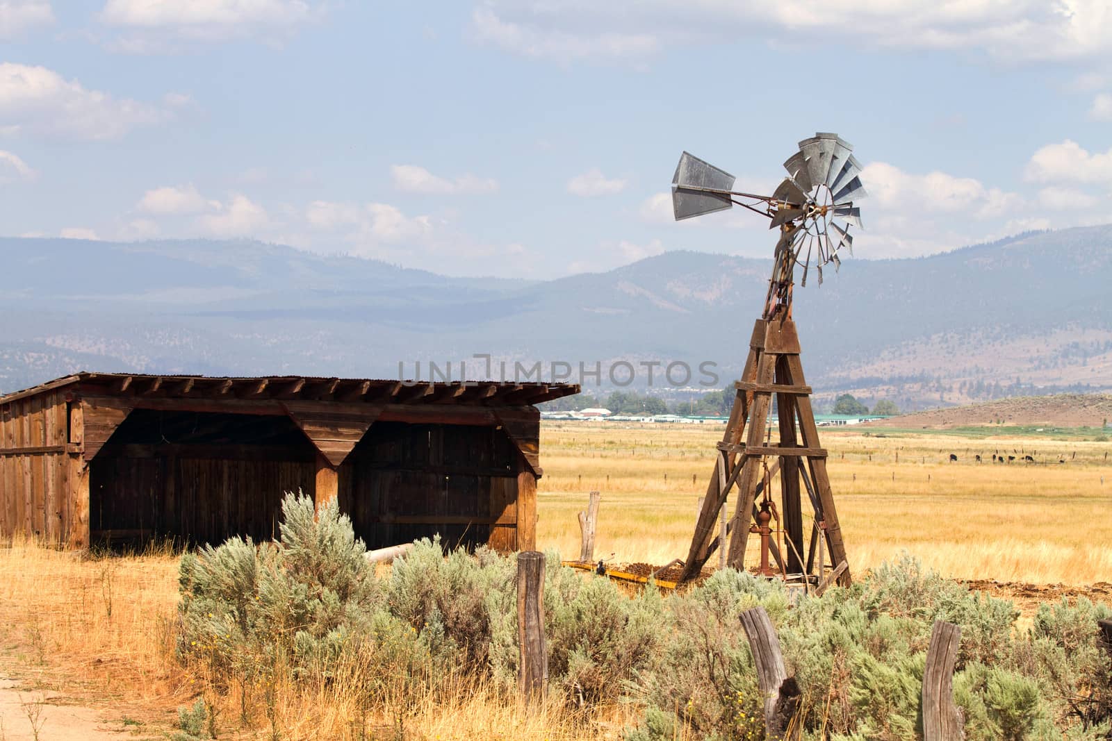 Old wind driven water pumping windmill stands next to an empty storage shed on a cattle ranch in a California mountain valley.
