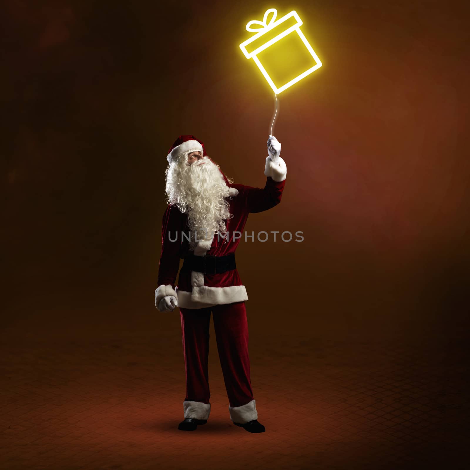 Santa Claus is holding a shining symbol of the gift on a string