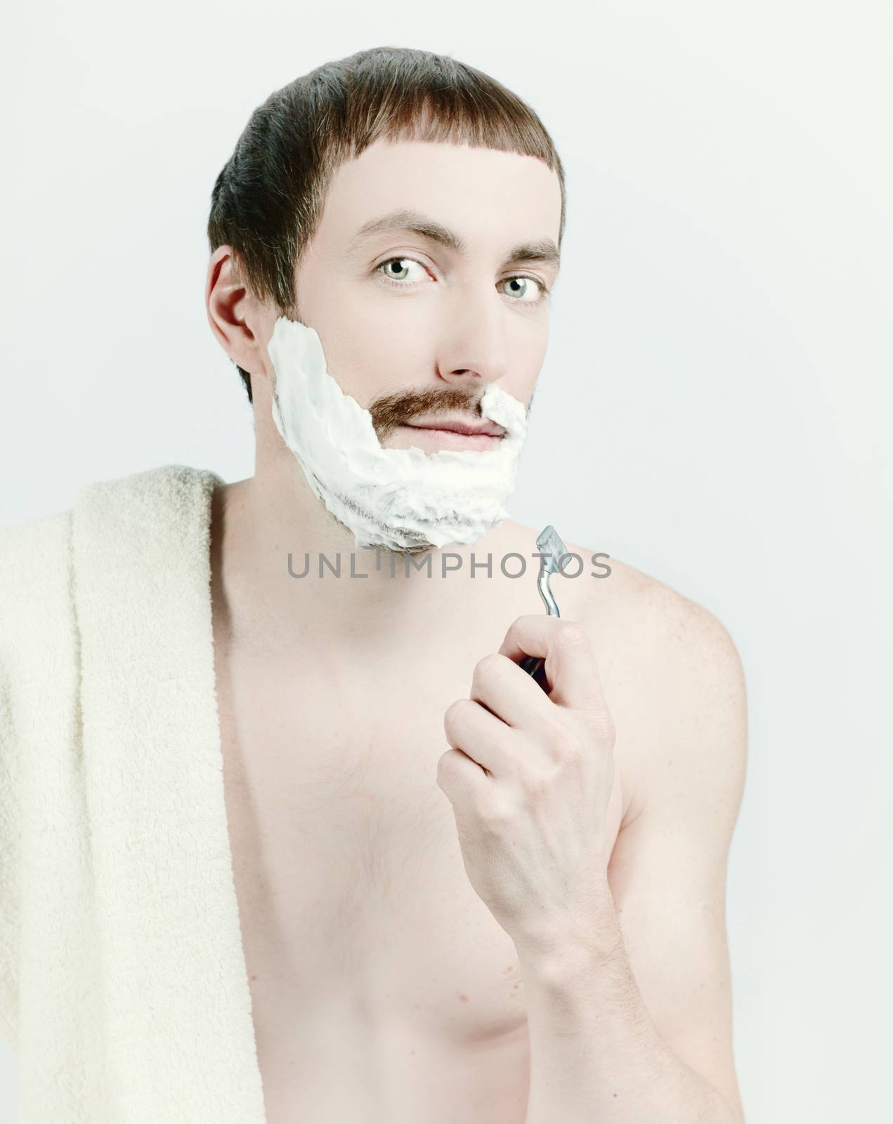 young man shaving with towel on the shoulders. 