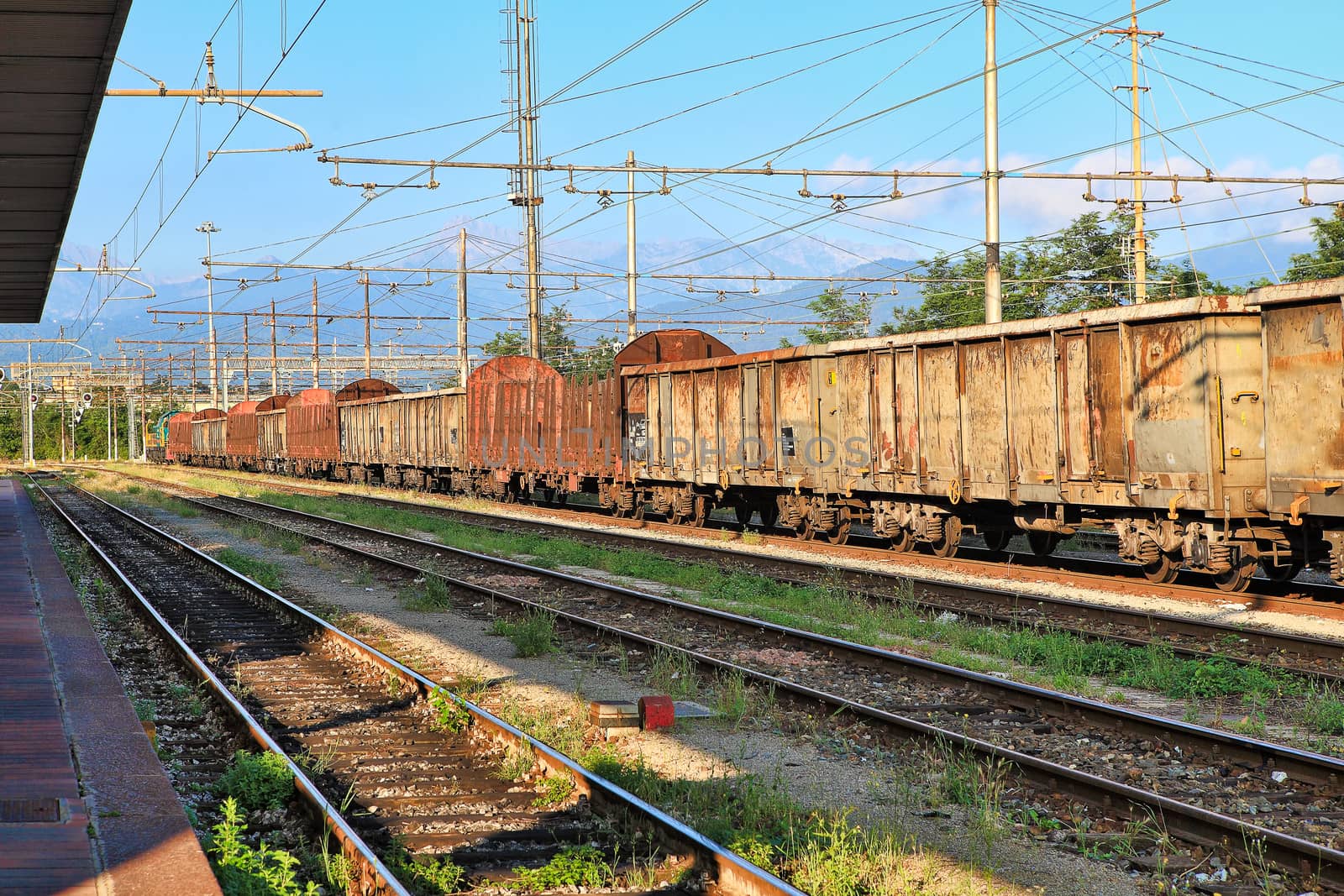 Old rusty freight cars stand on the track at the railway station.