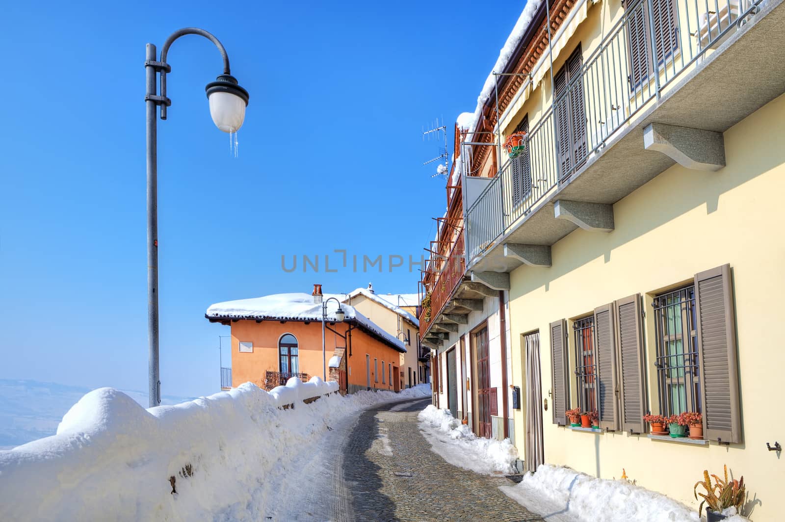 Narrow cobbled street covered with snow among lamppost and houses at town of Diano D'Alba in Piedmont, Italy.