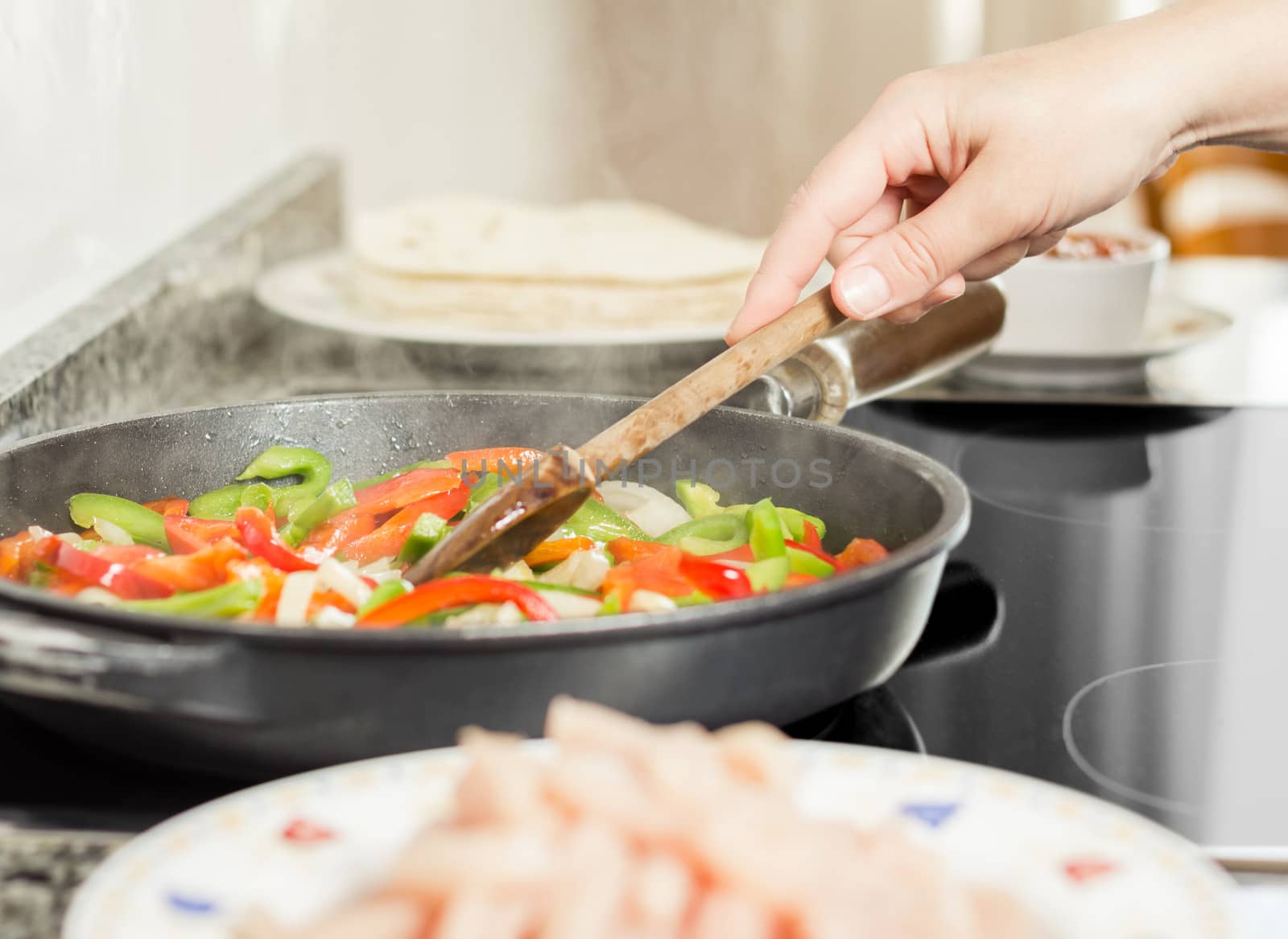 Closeup of female cooking vegetables and chicken for mexican food in a black pan