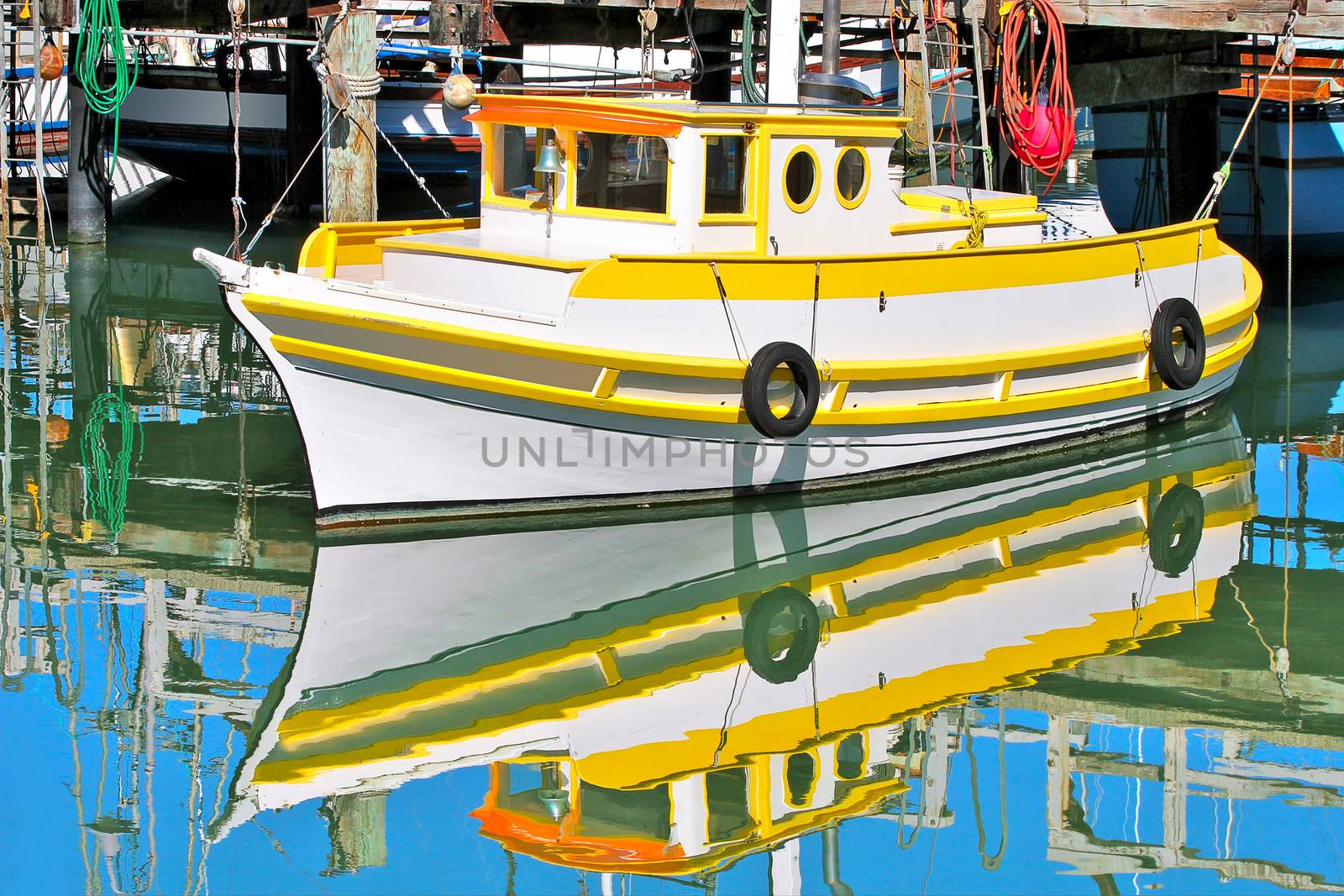 Yellow and white fishing boat moored at dock  and reflected with blue sky in the calm water of San Francisco marina in California, USA.