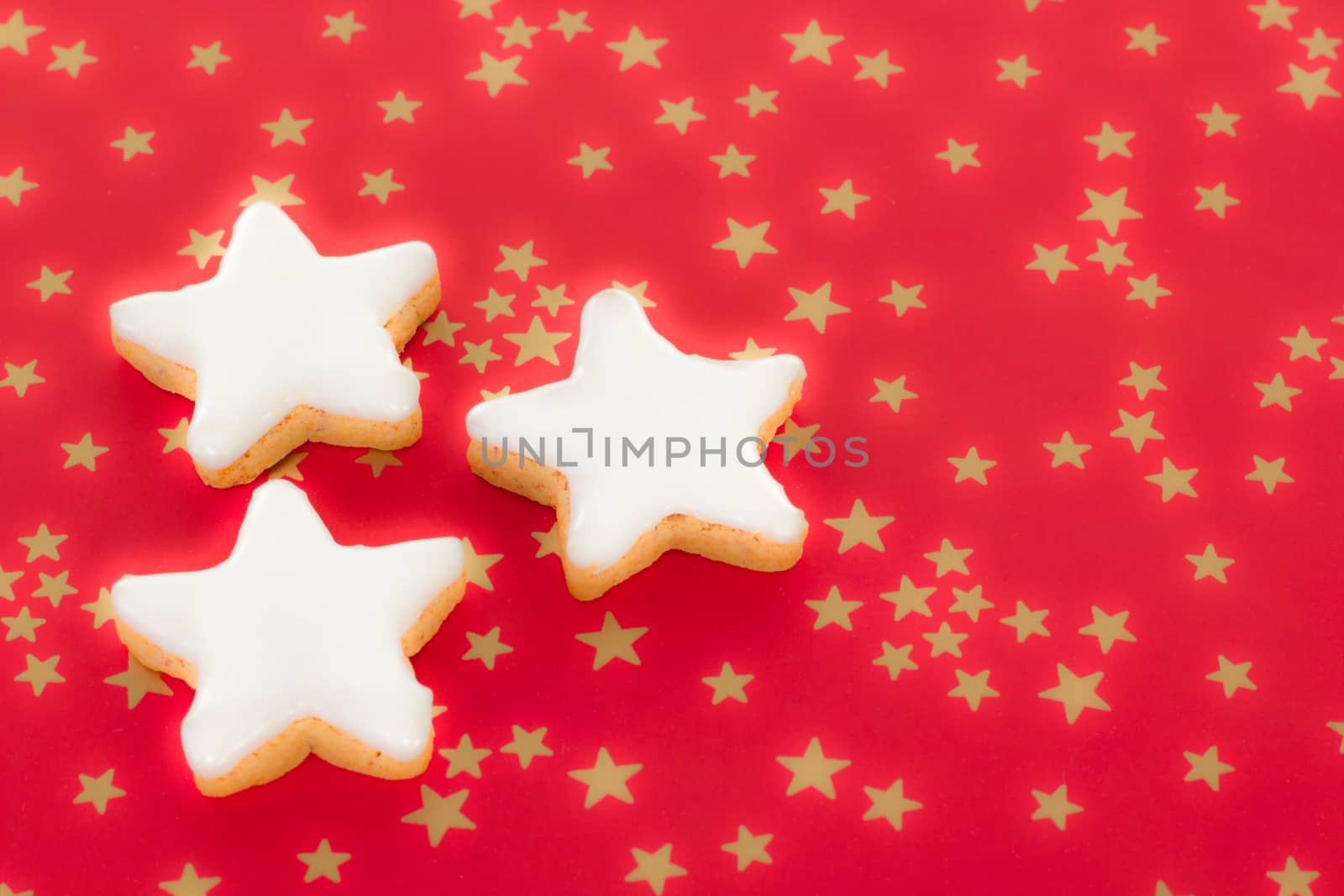Shining star shaped cinnamon biscuits on red background with golden stars