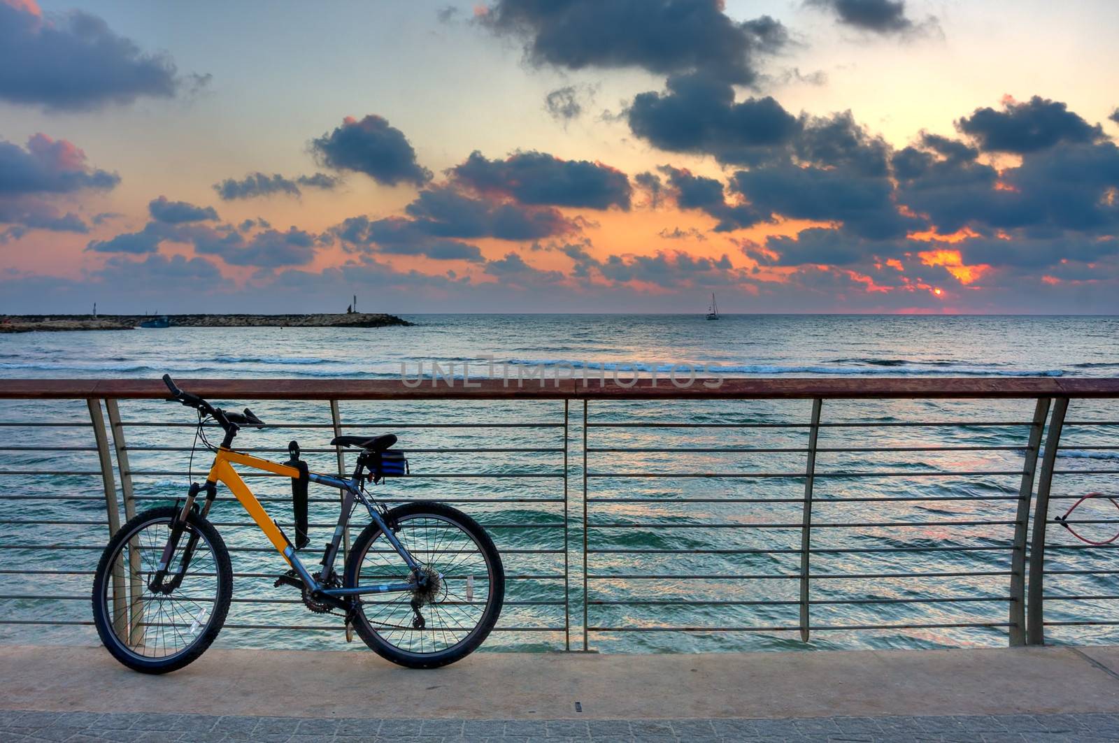 Bike on promenade against background of sunset sky and sea. by rglinsky