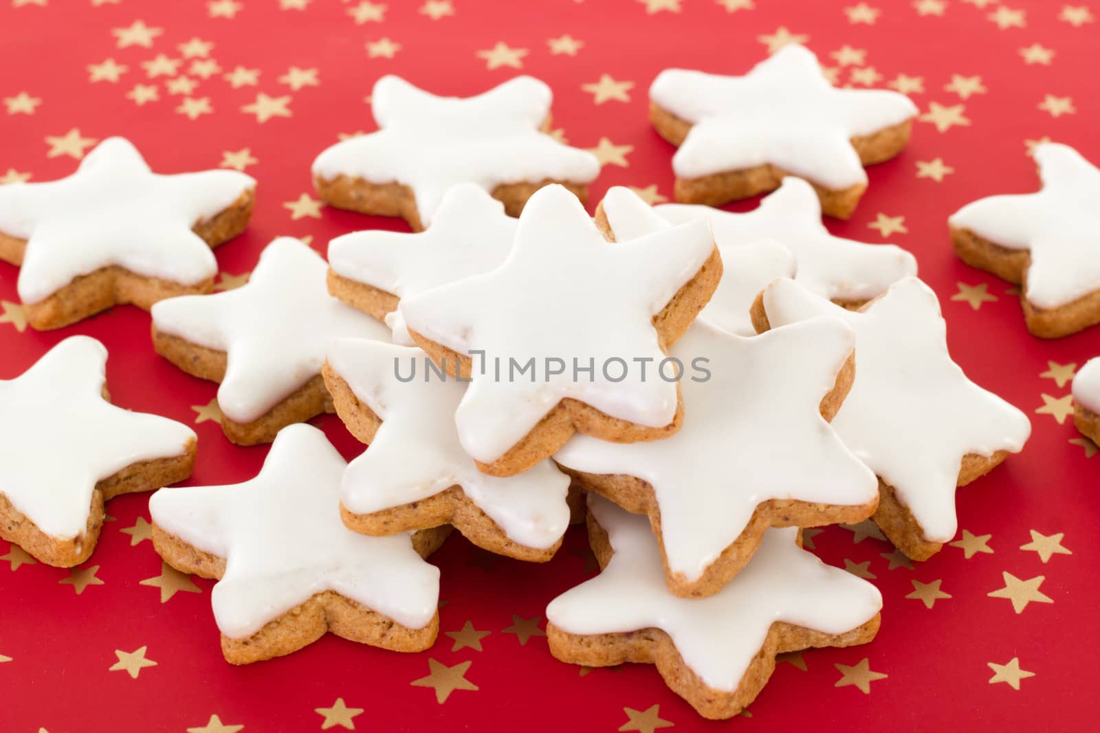 Star shaped cinnamon biscuits on red background with golden stars