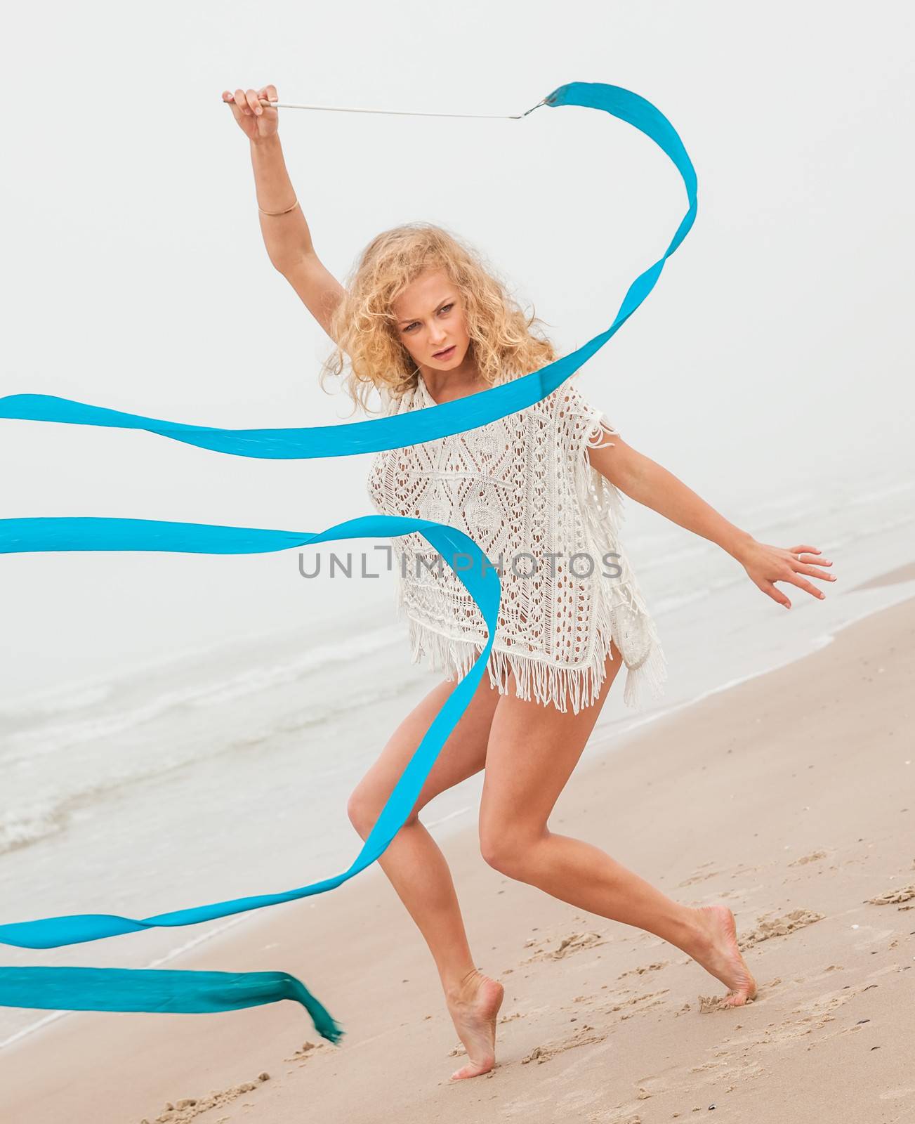 Young beautiful gymnast woman dance with ribbon on the beach at foggy day