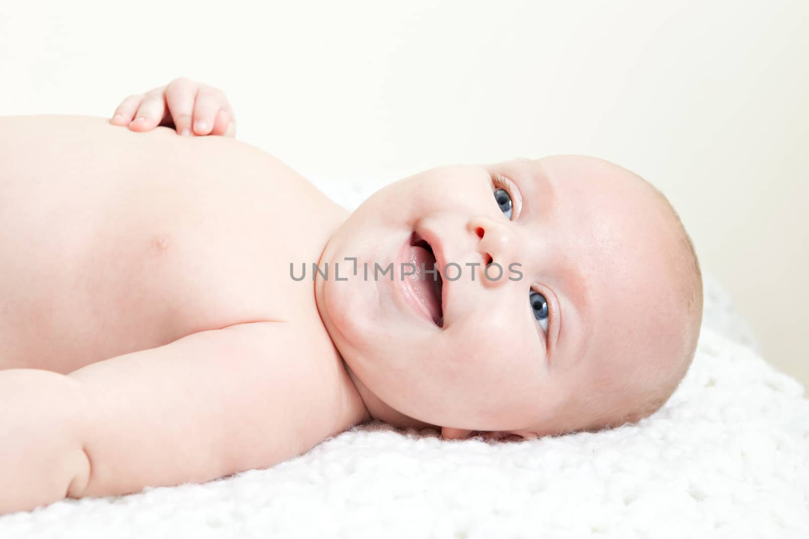 A cute newborn baby boy laughing and giggling while laying on his back.