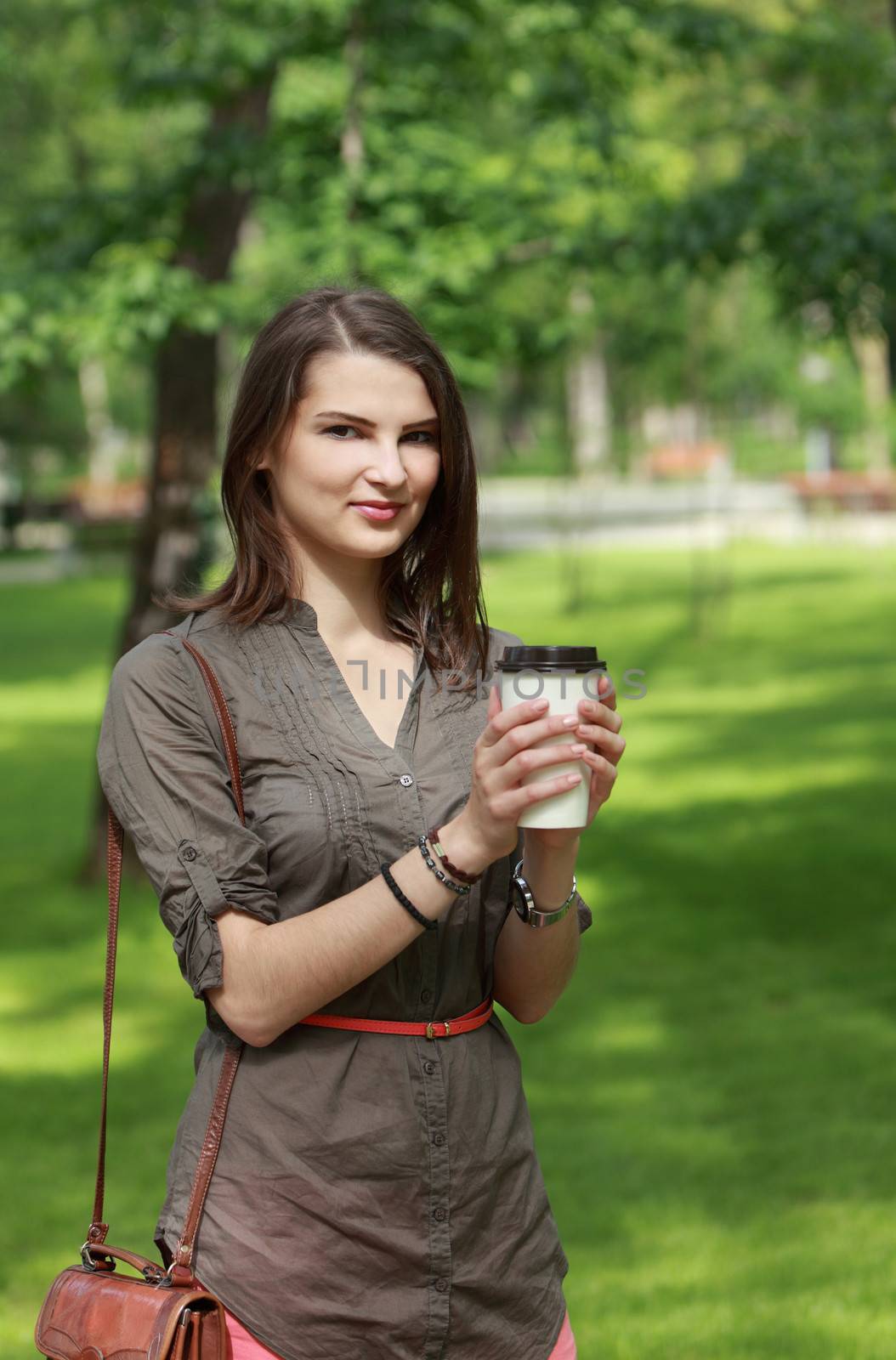 Portrait of a young woman holding a disposable cup of coffee outdoor in a park.