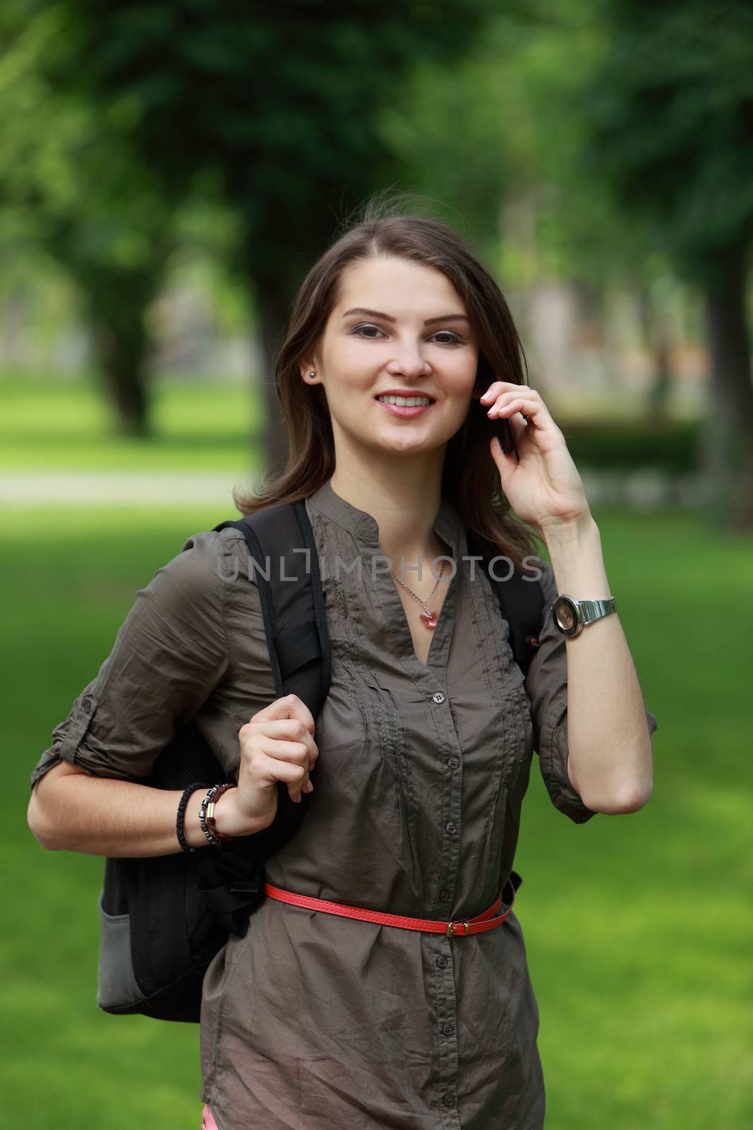 Young woman with backpack using a mobile phone in a park.